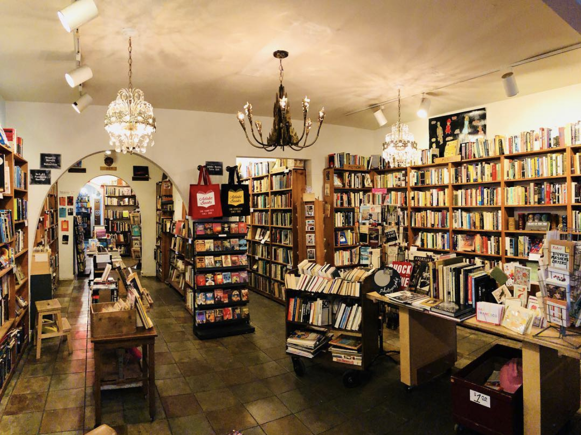 A musician performs at an album release party in a cozy bookstore filled with shelves of books.
