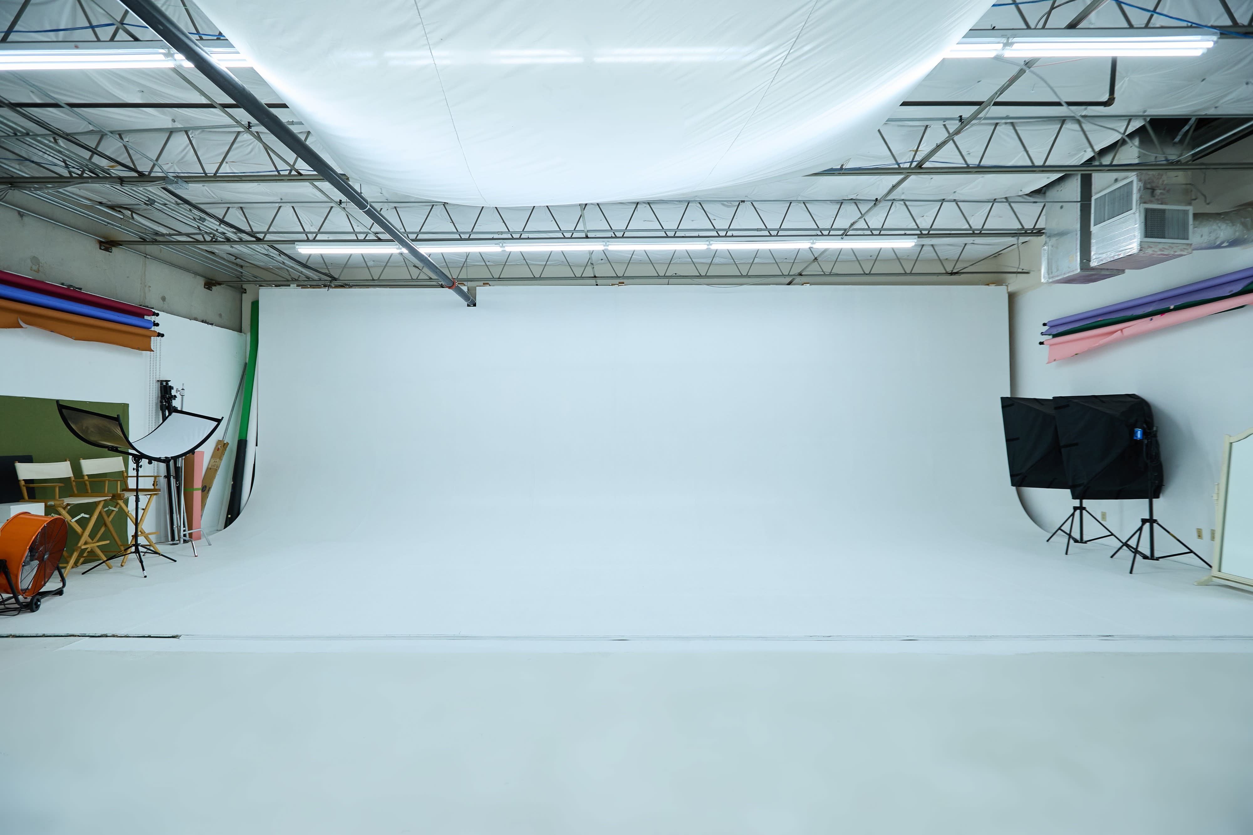 The image shows a video shoot setup in a studio with two chairs, lighting equipment, and a camera on a tripod.