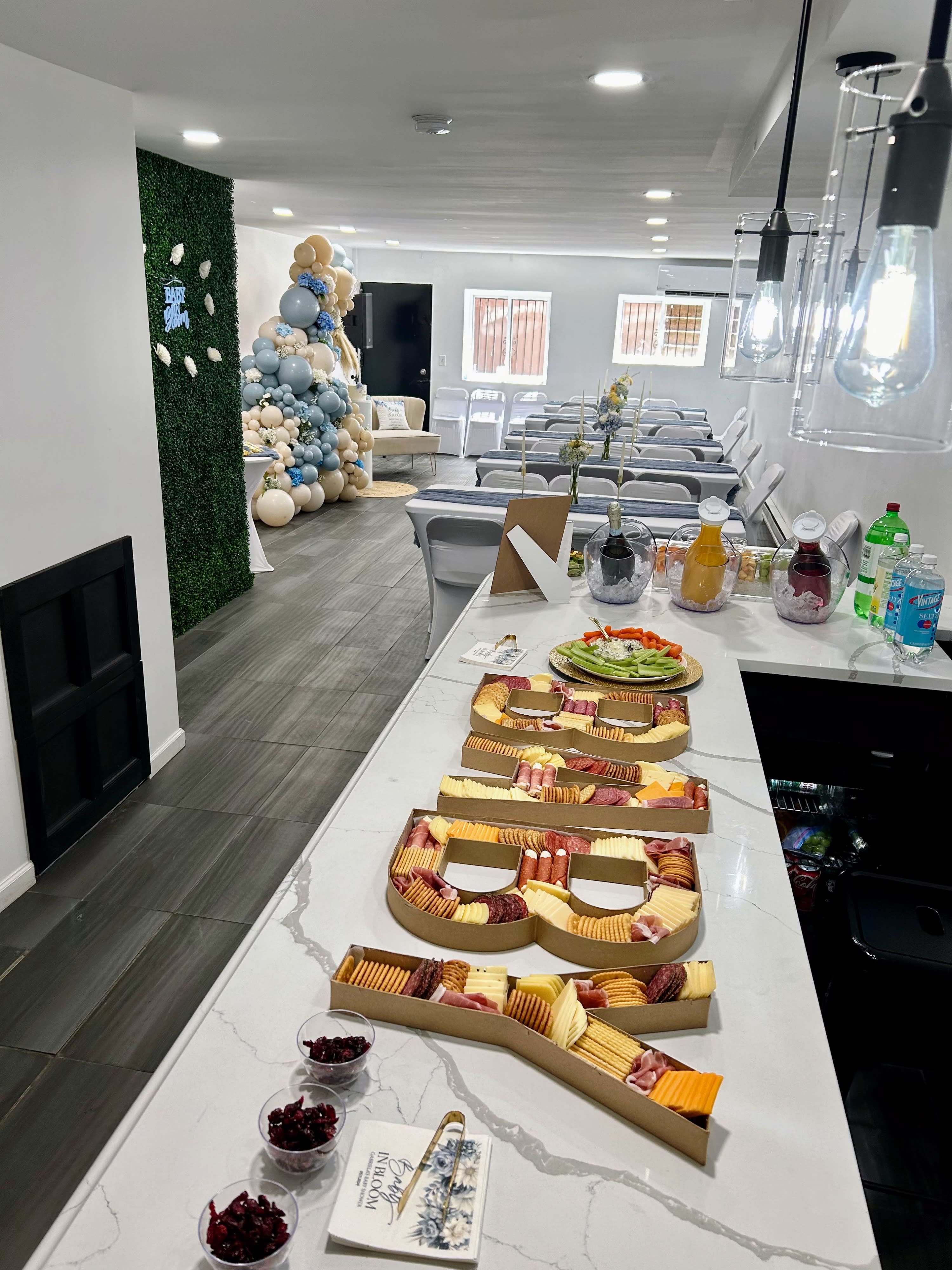 A table is adorned with a colorful spread of food, including a variety of cheeses, meats, fruits, and snacks, decorated with greenery for a birthday celebration.