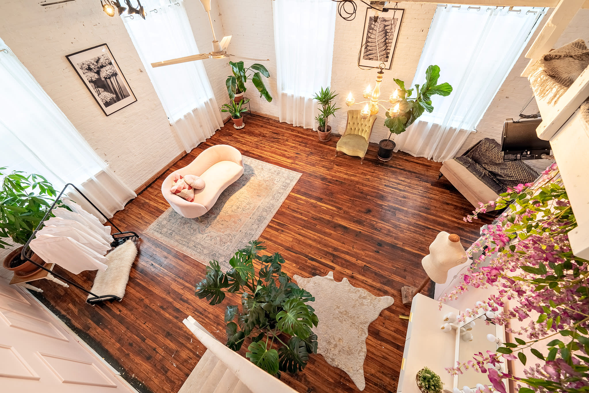 A cozy production set features a tastefully arranged area with a decorative table, comfortable seating, and a teepee, surrounded by plants and natural light.