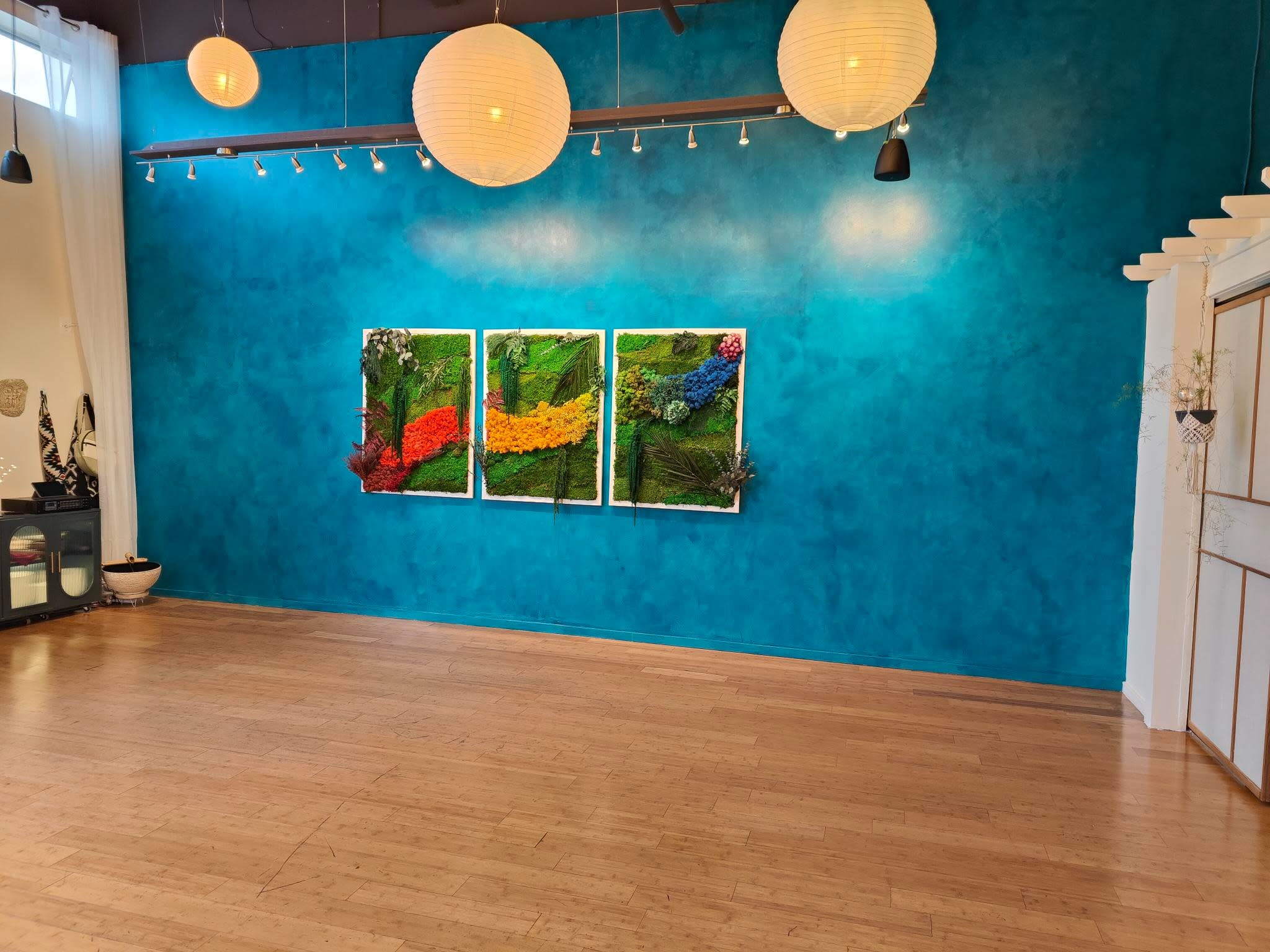 The image shows a yoga studio arranged with mats and props, ready for a class, beneath hanging lanterns and artwork on the walls.