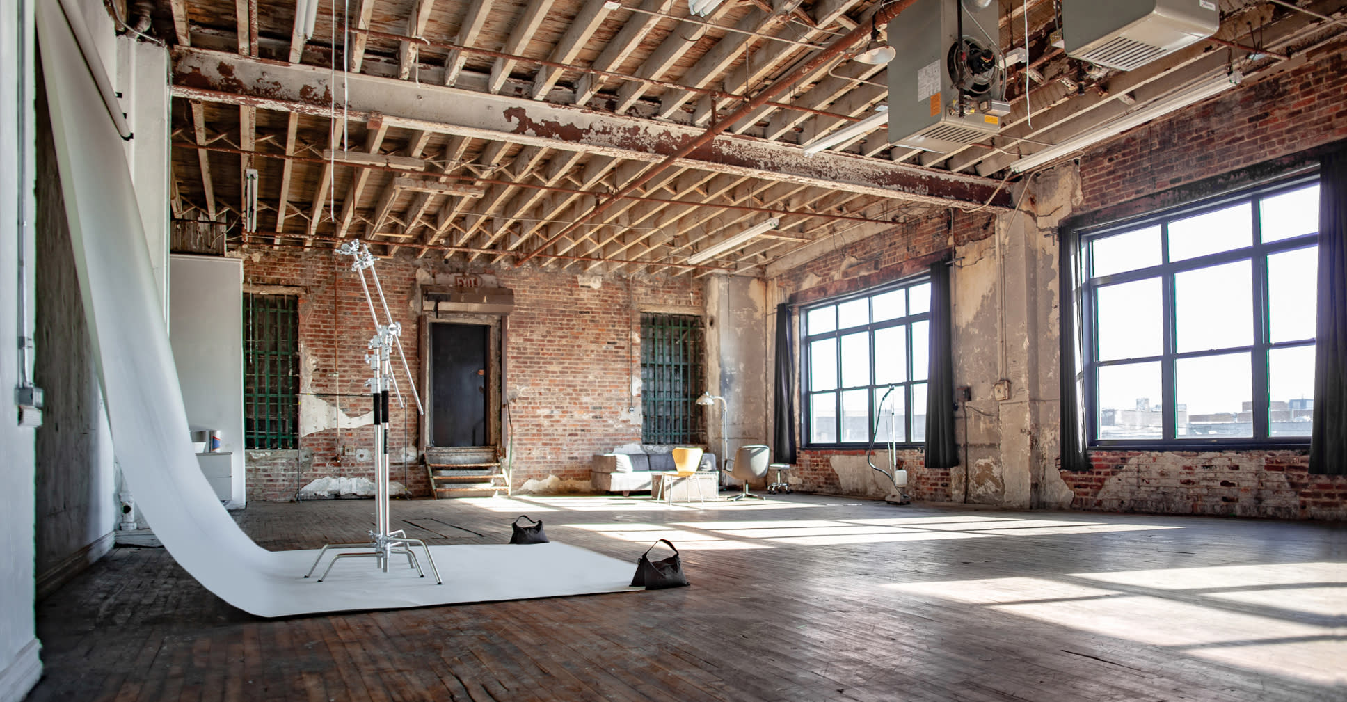 A subject sits on a stool in front of a backdrop, illuminated by studio lights in a spacious, industrial-style room.