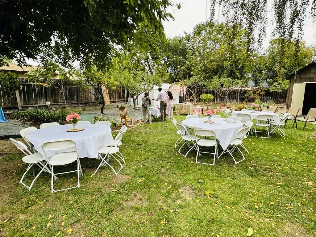 A long dining table is set outdoors for a birthday celebration, adorned with floral centerpieces and elegant tableware.