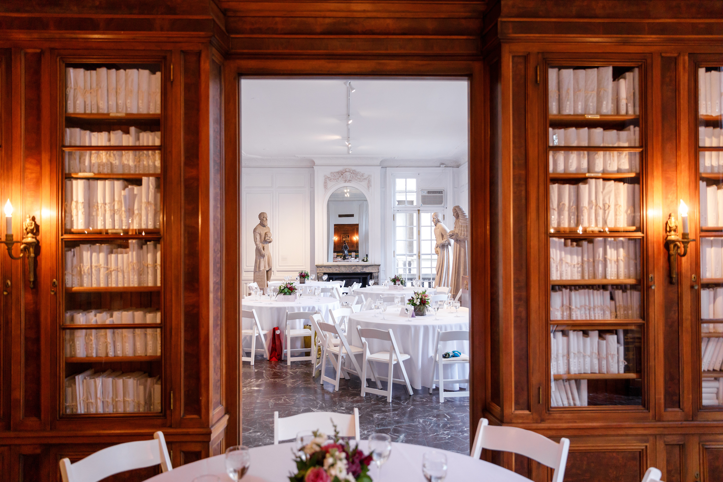 A decorative pedestal holds a floral arrangement alongside lit candles, set against a backdrop of large windows.