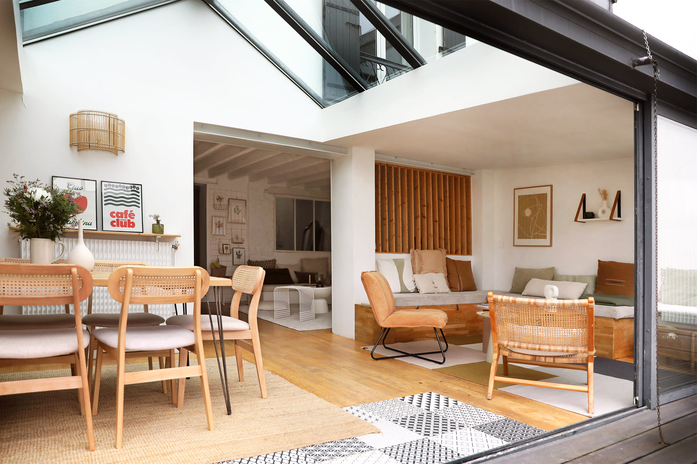 A dining area with a wooden table and chairs overlooks a landscaped outdoor space through glass walls.