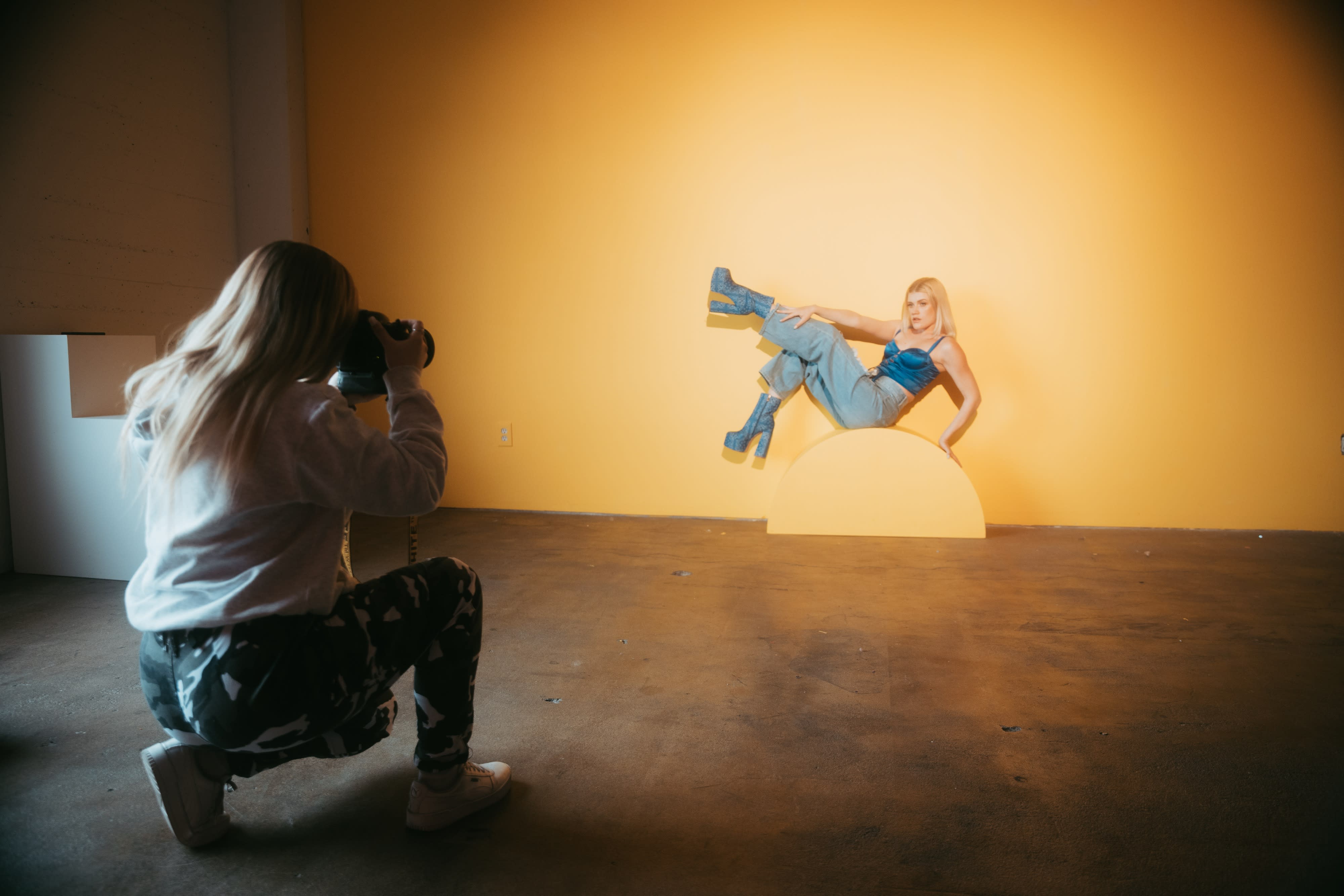 A model poses confidently in front of a shimmering silver backdrop during a video shoot.