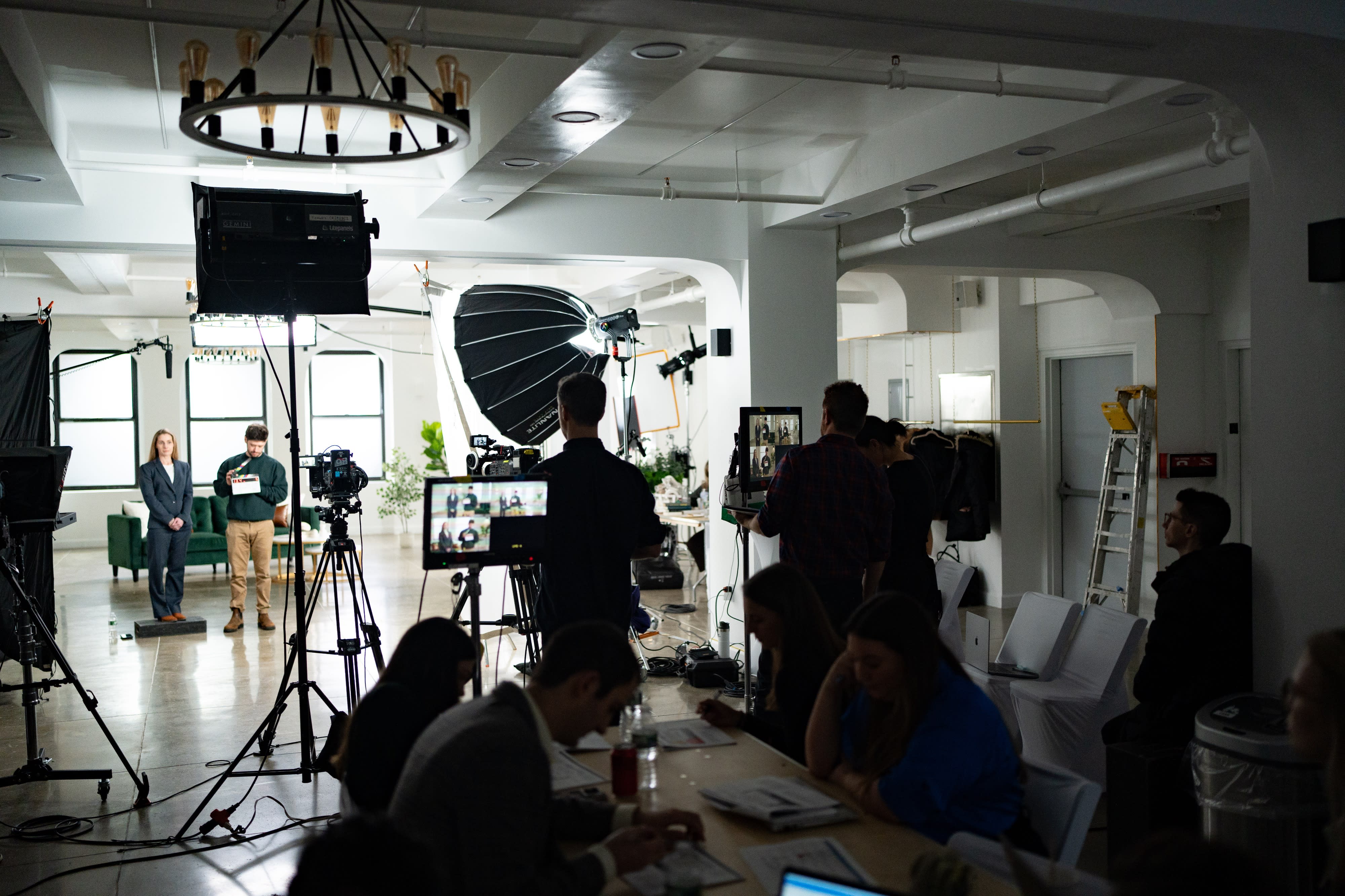 A film crew is capturing a scene with two presenters in a well-lit studio set.