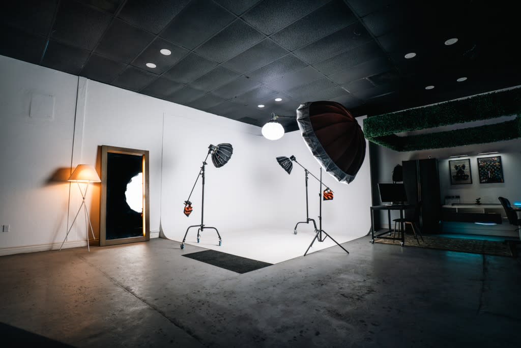 A model poses in a studio setting, seated on the floor against a plain backdrop while adjusting her hair.