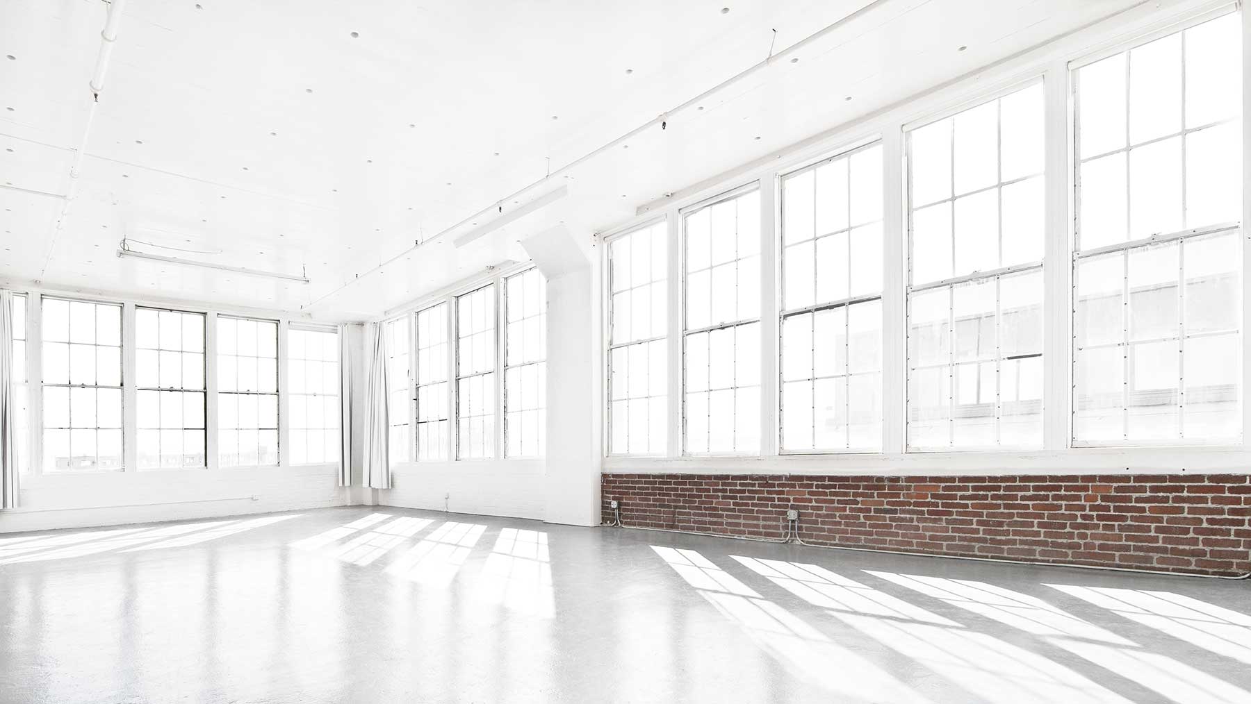 A heart-shaped arrangement of white flowers occupies the center of a sunlit, empty room with large windows overlooking the city.