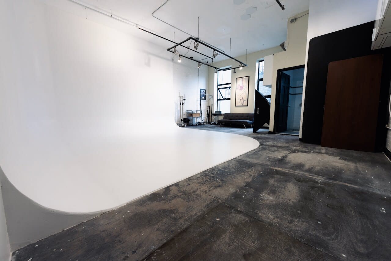 A photographer captures a subject posing against a plain white backdrop while standing on a ladder.
