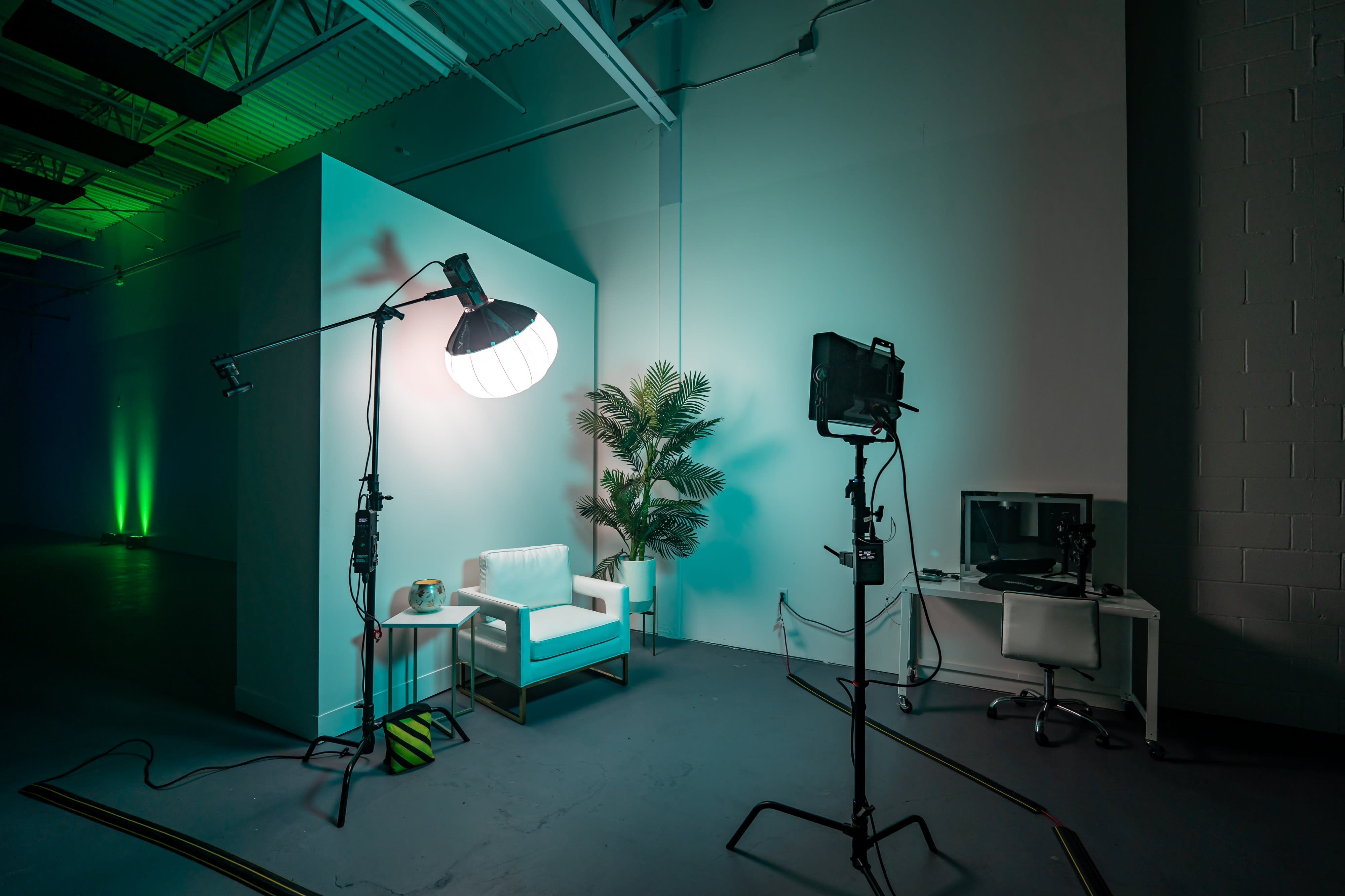 A crew member operates a camera while another individual stands in front of a backdrop, preparing for a talking head interview shoot.