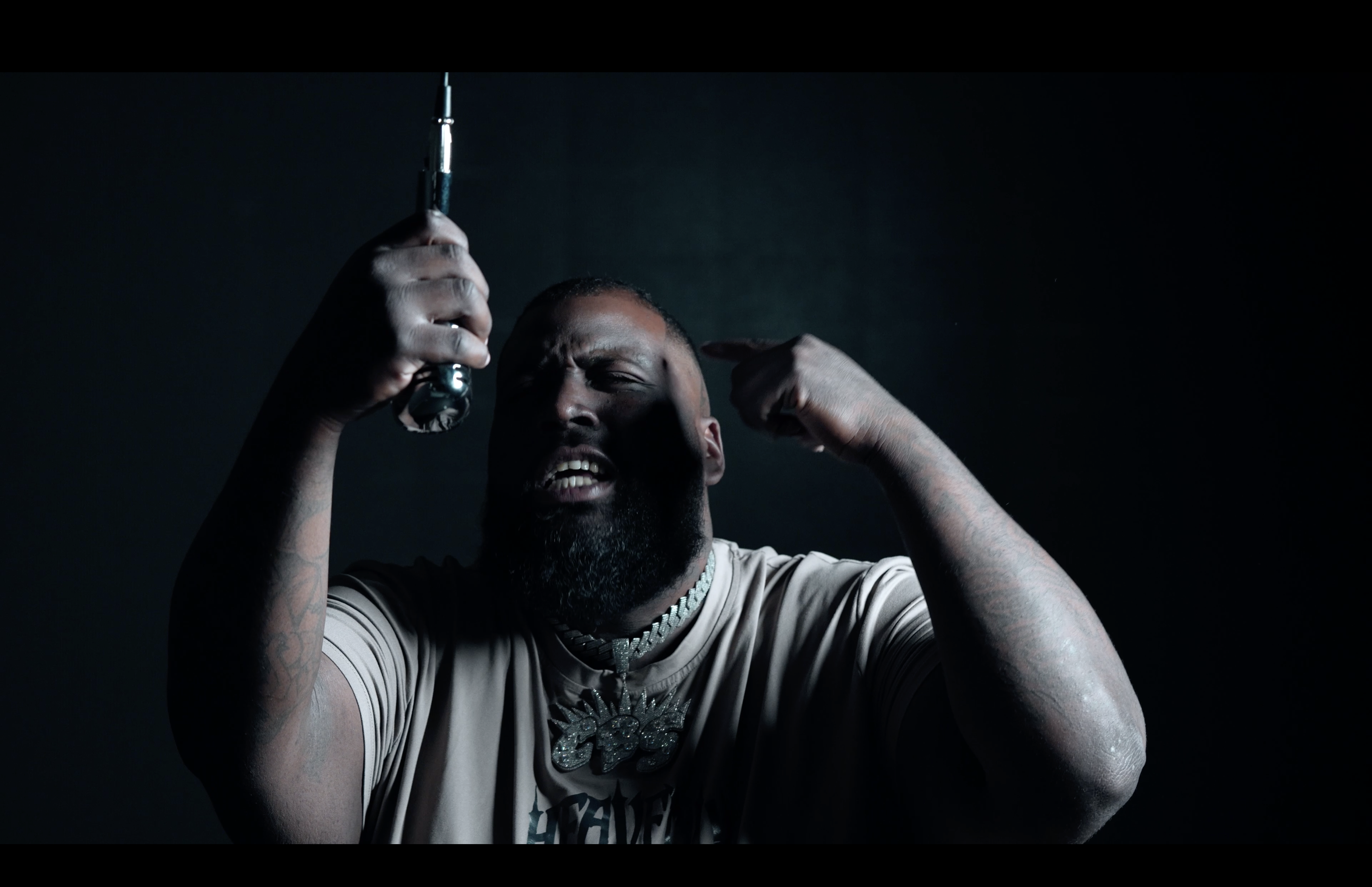 A performer walks confidently down a narrow hallway lit with vibrant purple and blue lights, holding a bat amidst a smoky ambiance during a video shoot.