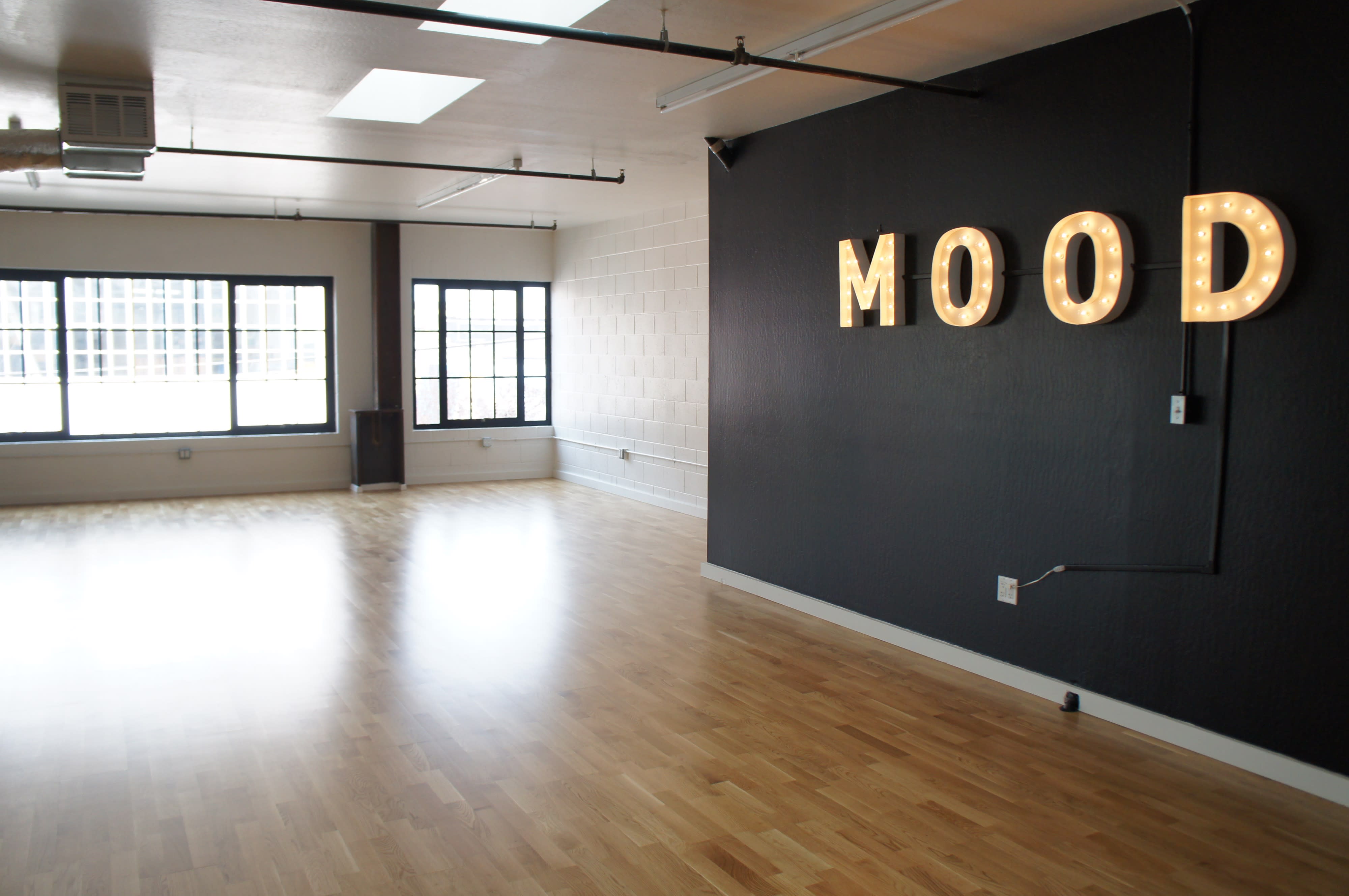 A group of twelve dancers in white shirts poses confidently in front of a large "MOOD" sign during a workshop.