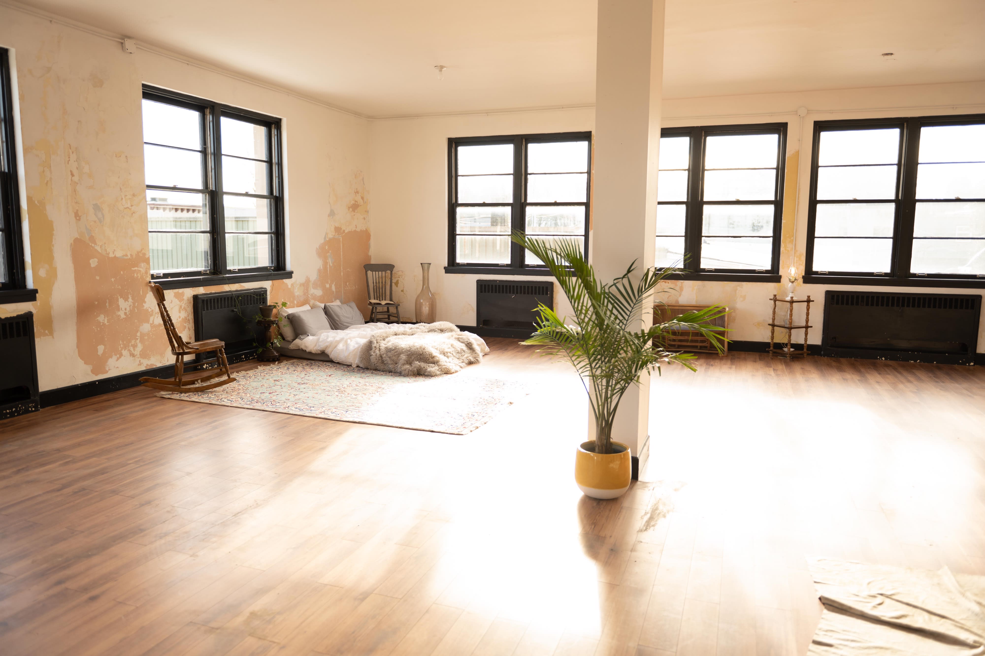 A person performs an inverted pose on a rug in a sunlit room with large windows.