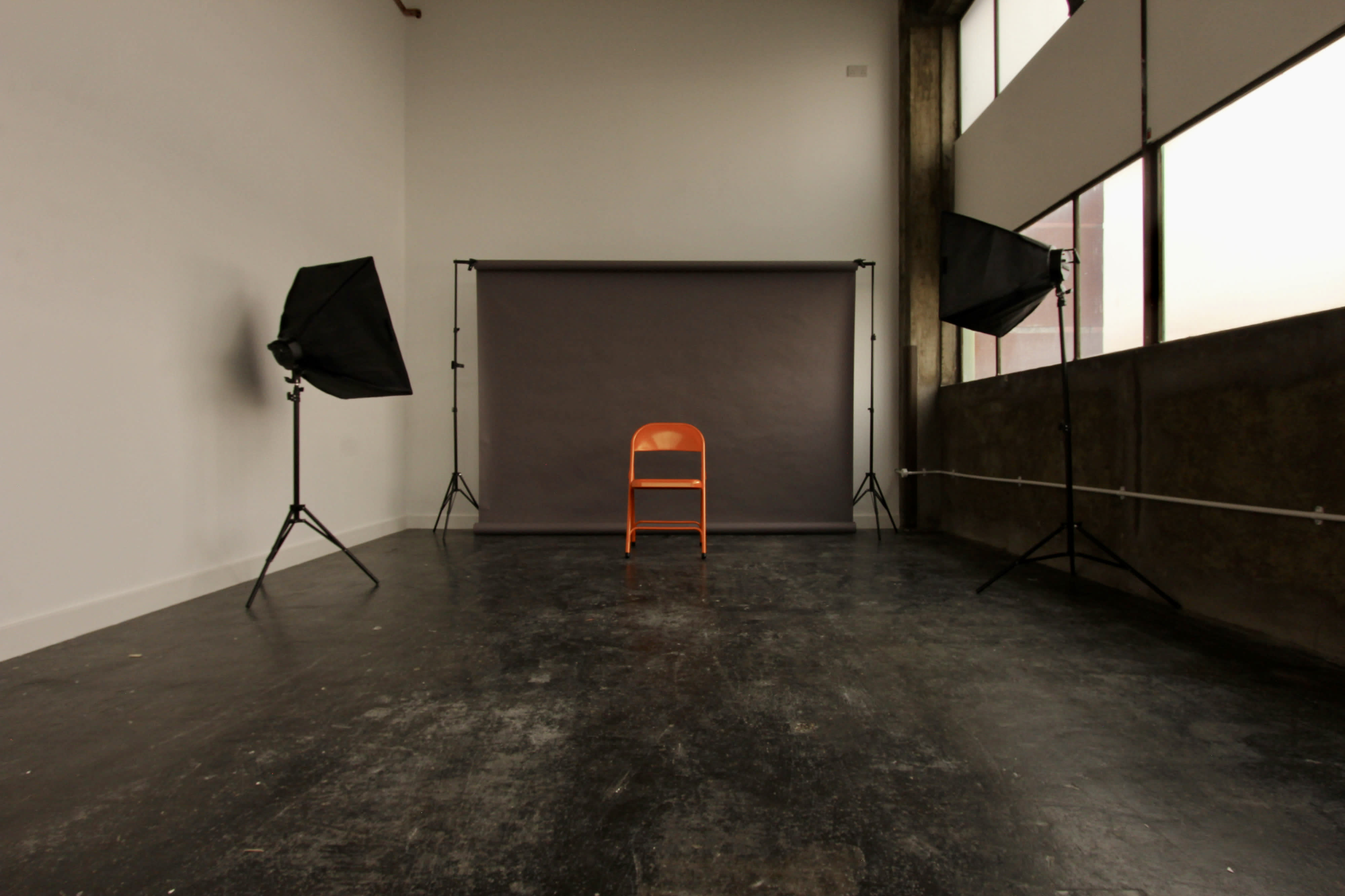 A model poses casually while sitting on a ledge in a photo studio, wearing oversized clothing and work boots.