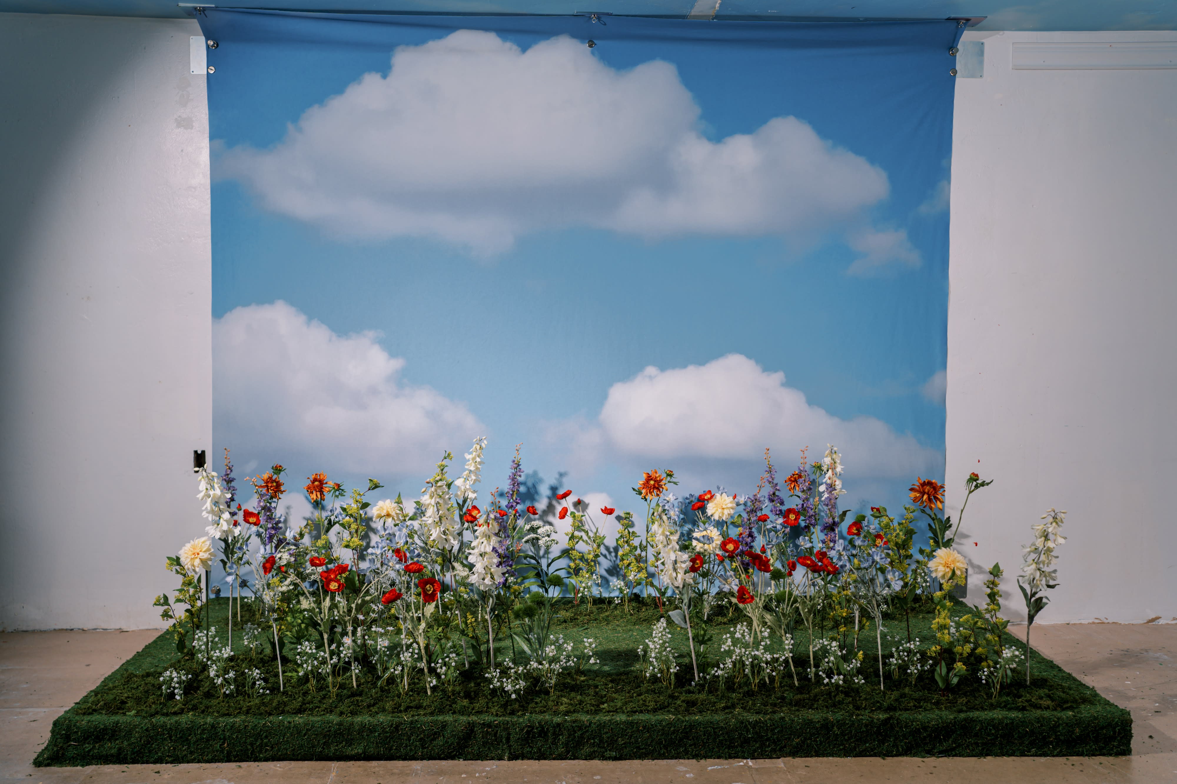 A model poses with a floral embroidered veil against a backdrop of blue skies and clouds.