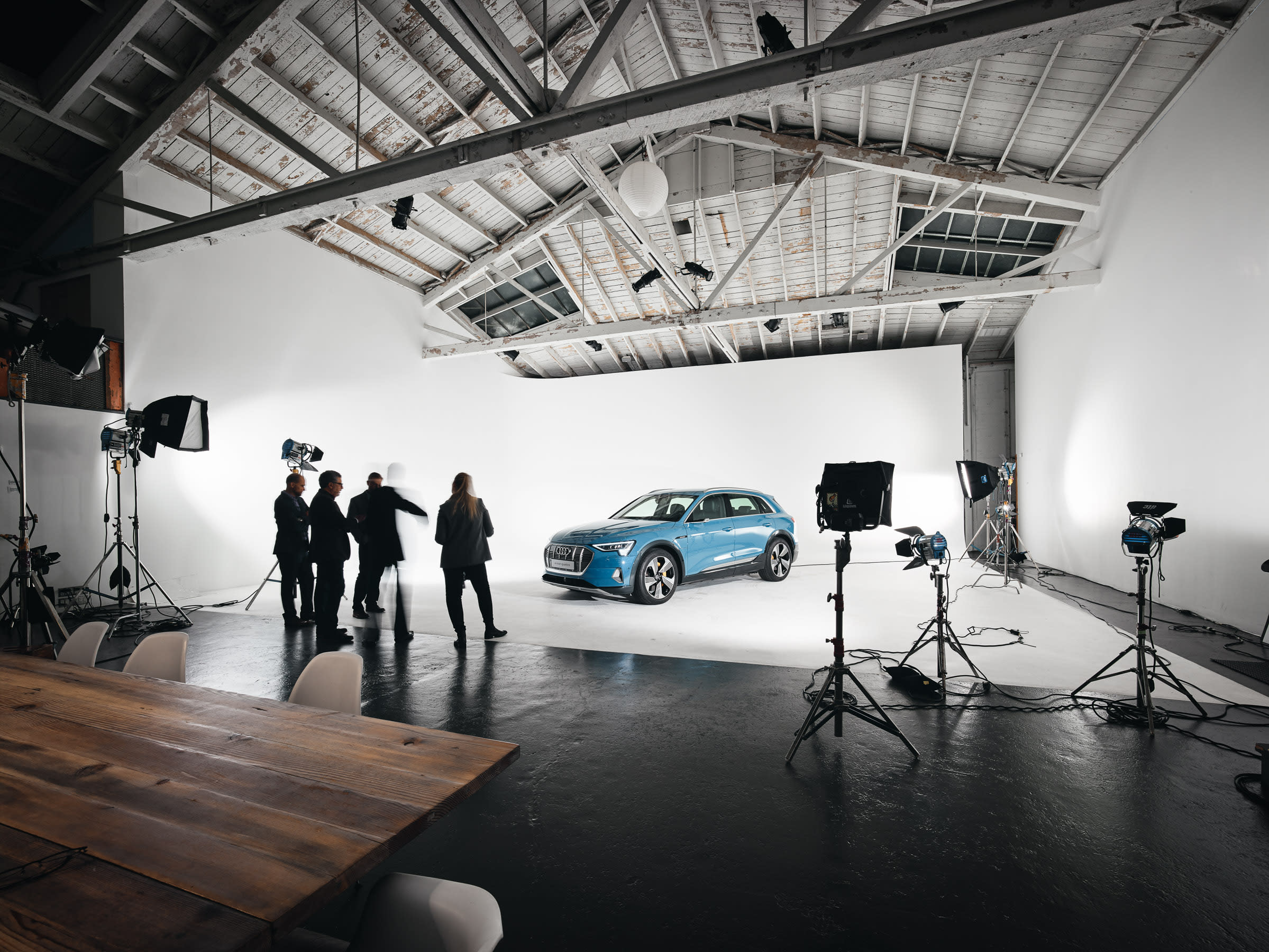 A video shoot takes place in a well-lit studio featuring two softbox lights and a rectangular frame suspended from the ceiling against a plain backdrop.