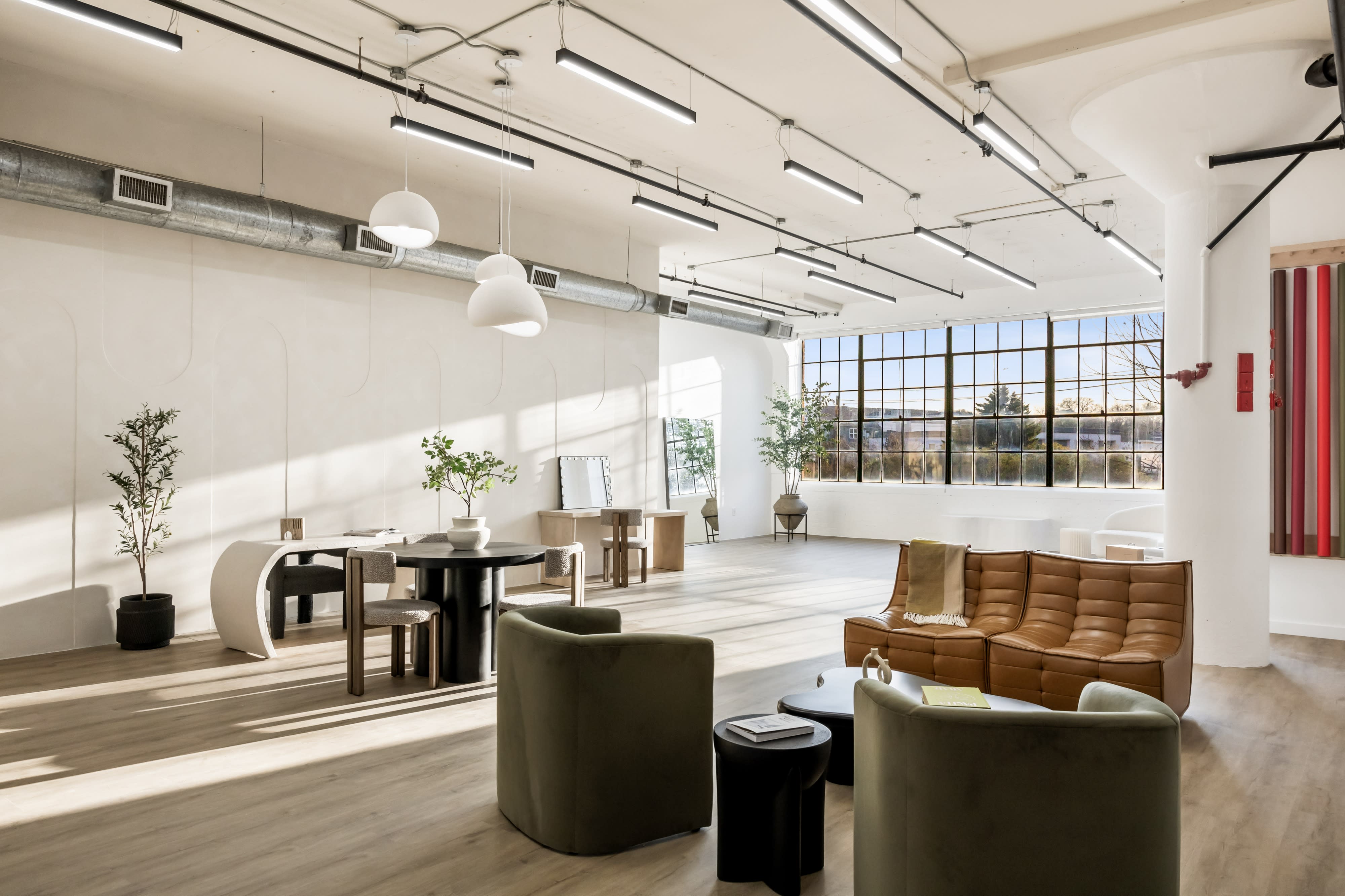 A spacious, well-lit studio features a cozy couch and large window casting natural light across the wooden floor.