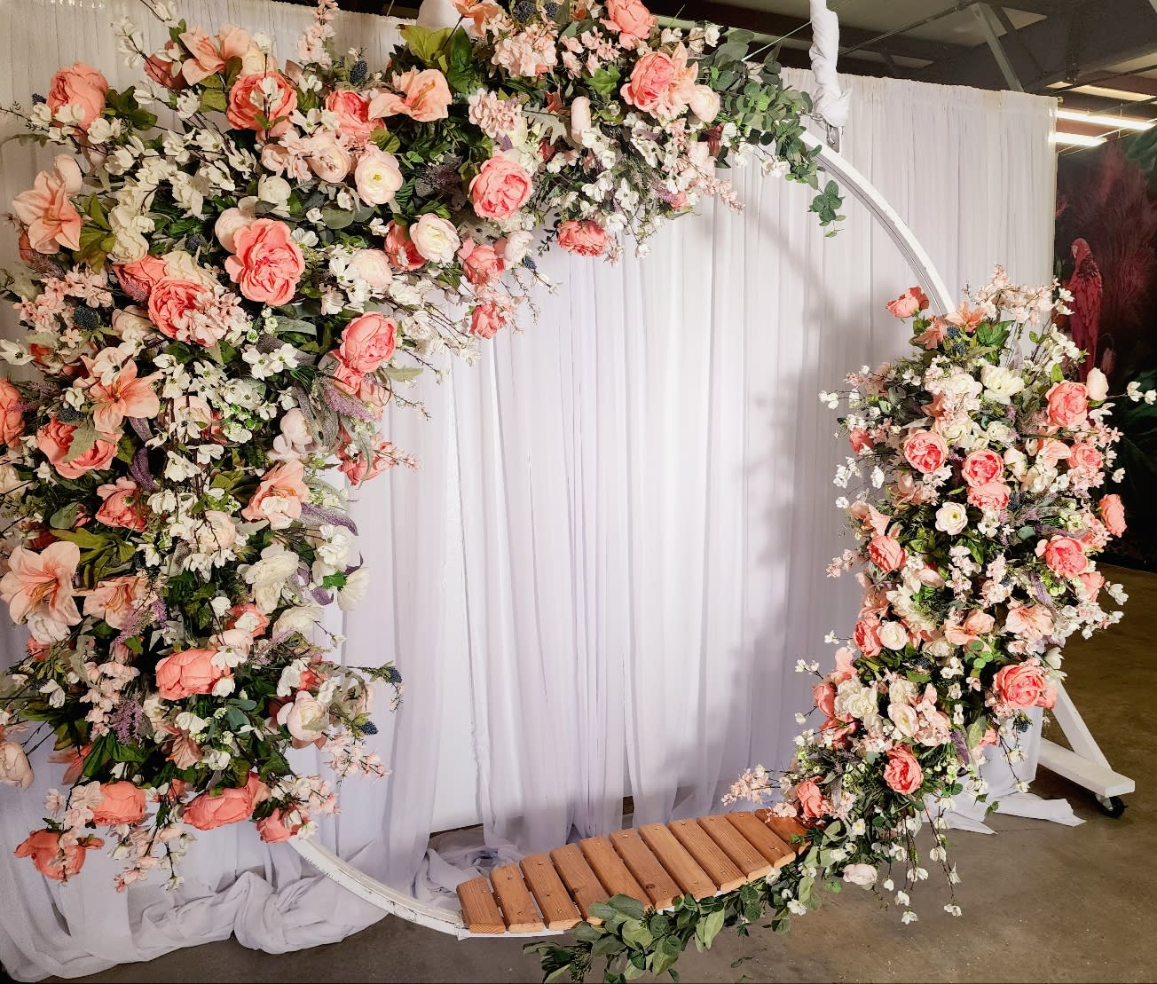 A bride stands by a large window, holding a bouquet of flowers while wearing a detailed wedding gown.