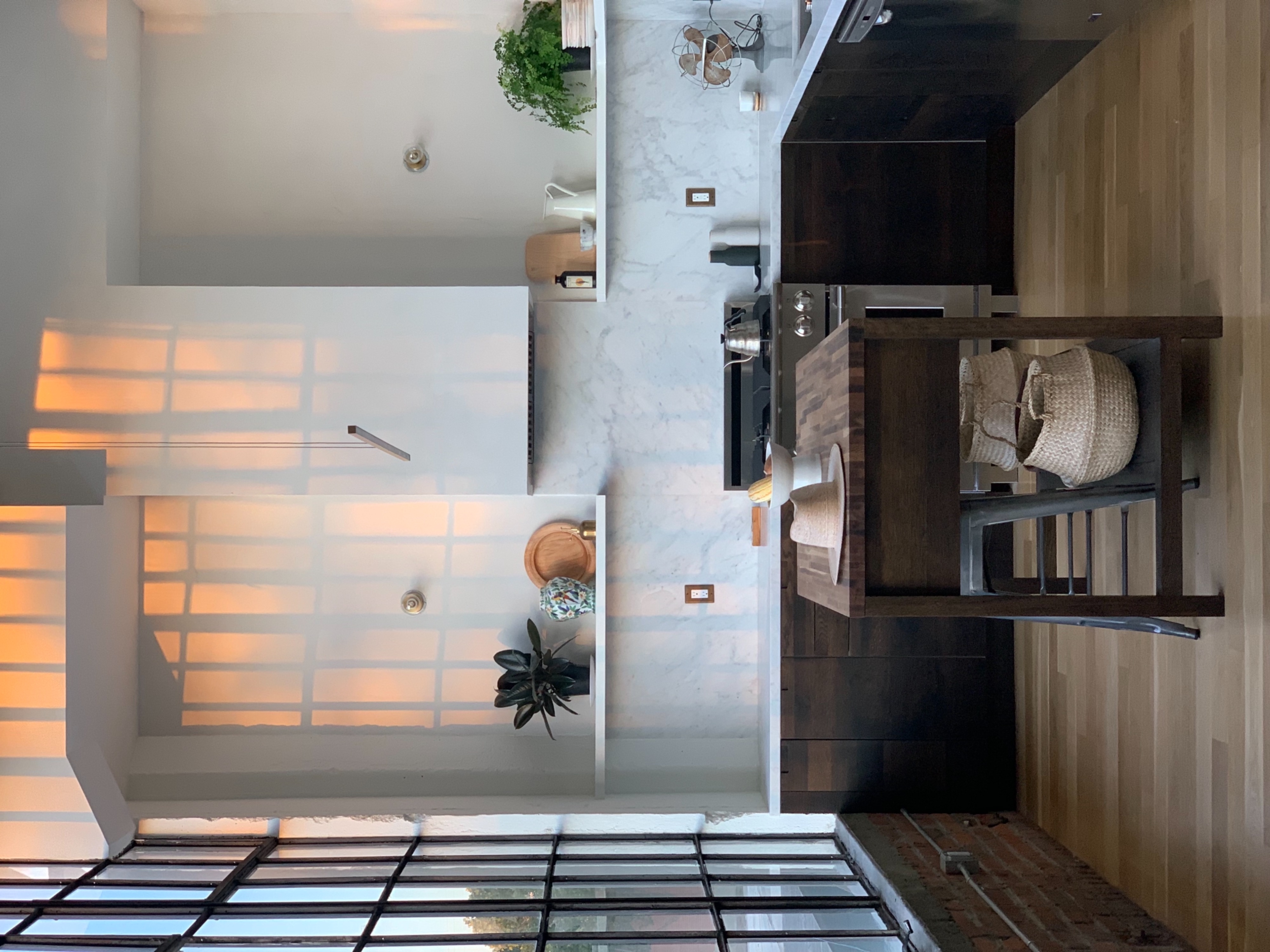 A woman works on a laptop at a wooden kitchen table in a bright, spacious kitchen.