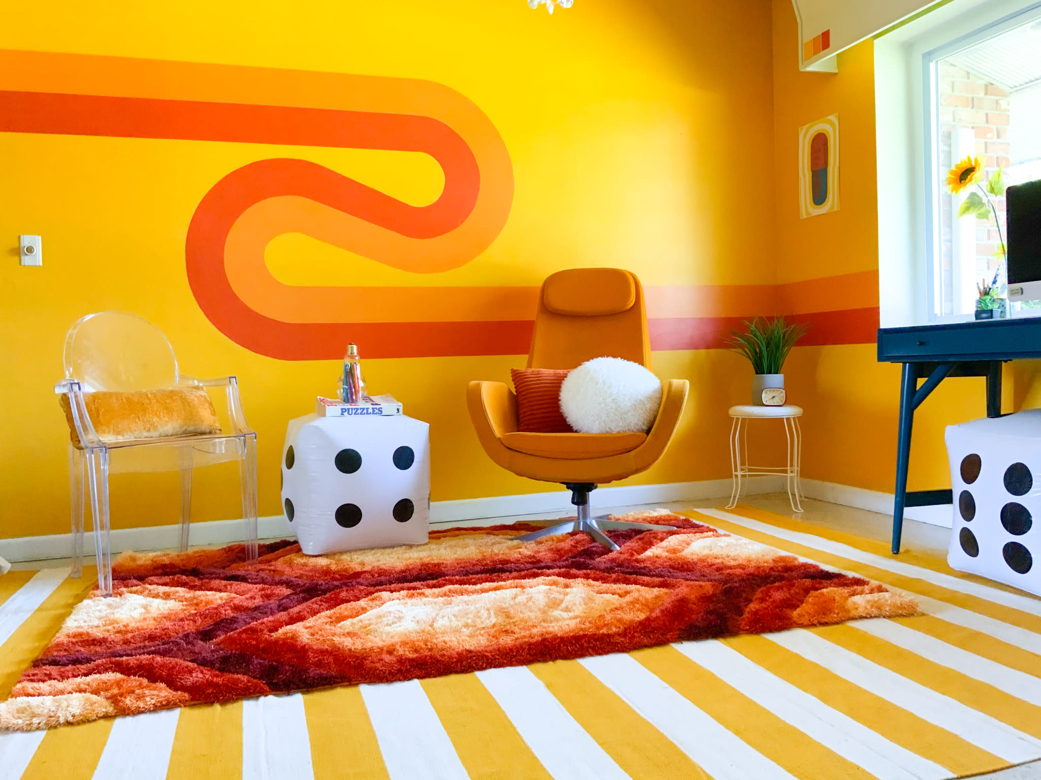 A woman sits on a velvet couch in front of a colorful wall adorned with vintage posters and a table featuring board games.