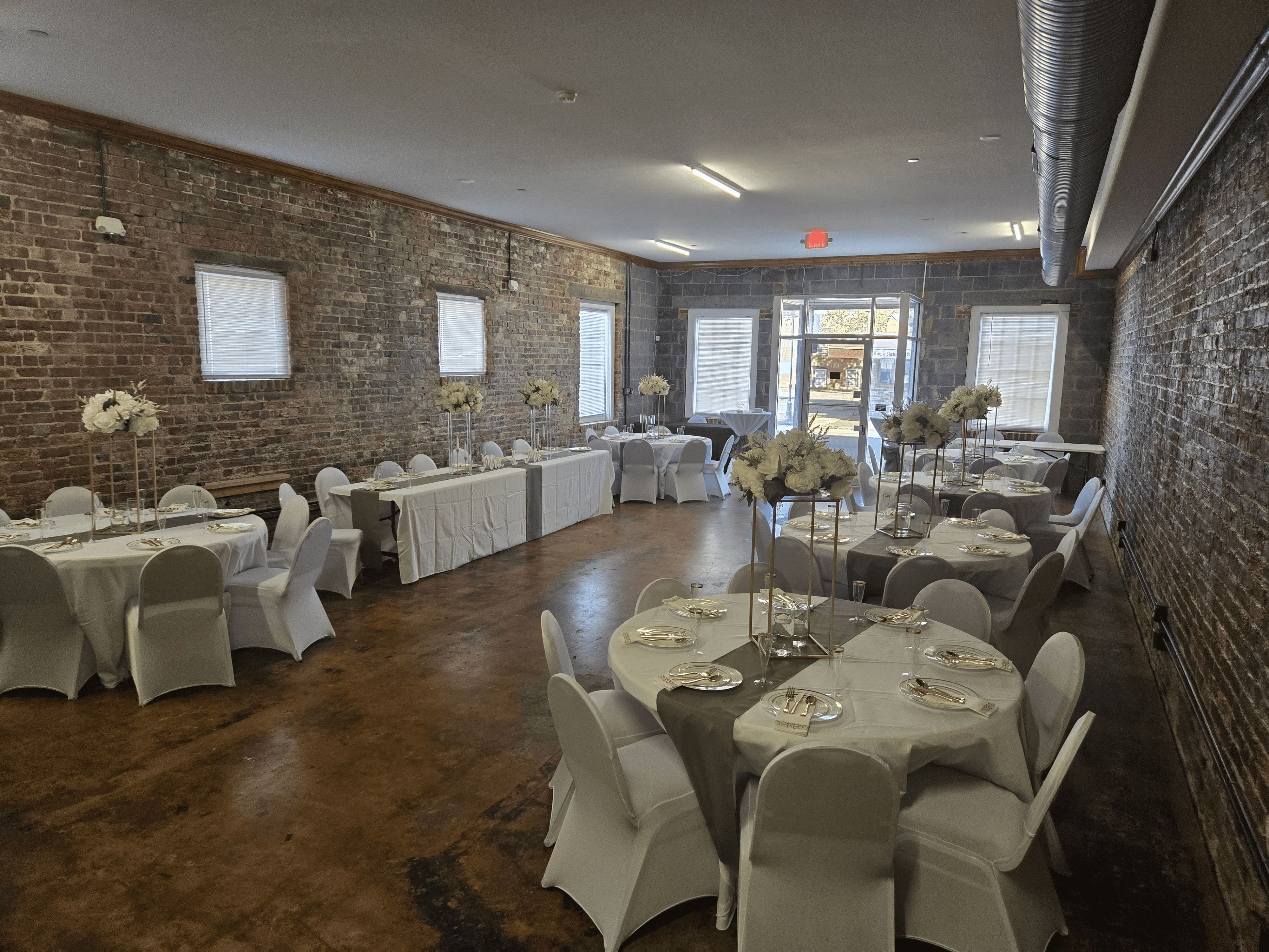 A beautifully decorated baby shower table features a pastel-themed setting with floral centerpieces and a buffet spread against a brick wall.