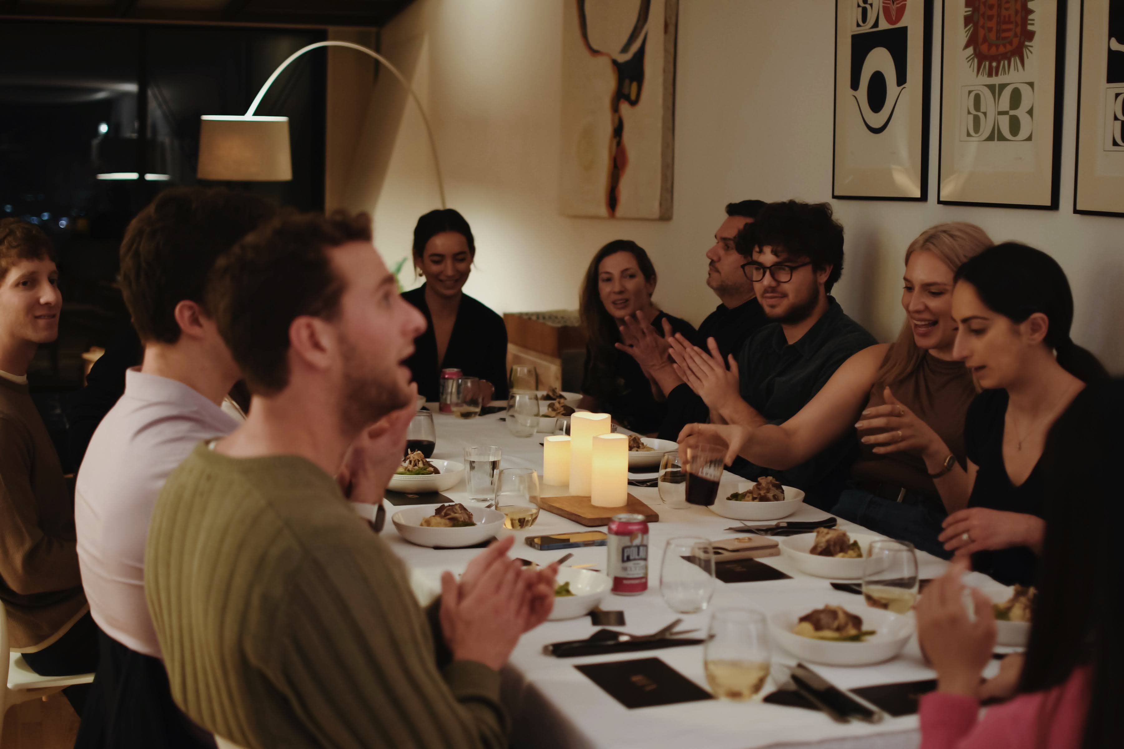 A long dining table is set with elegant tableware, wine bottles, and floral arrangements in preparation for a dinner gathering.