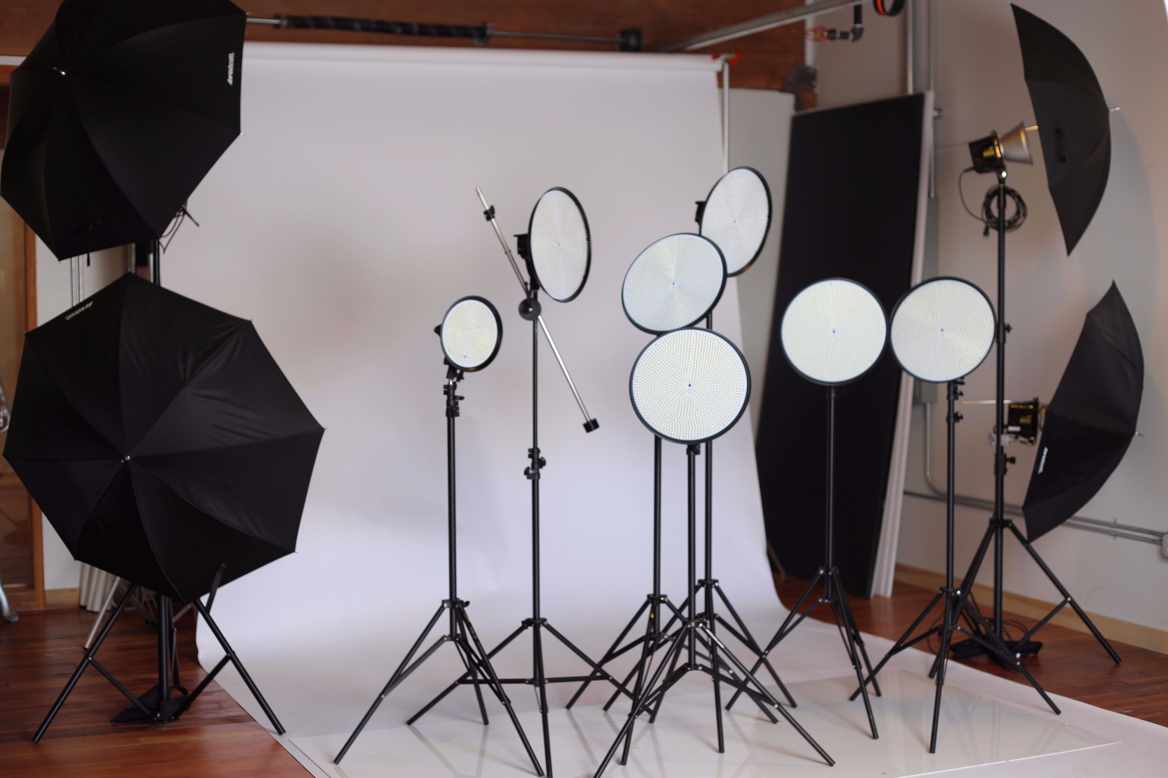 The scene features a photo shoot setup with a beige backdrop, white draped table, and various candles arranged on the table, illuminated by multiple softbox lights.