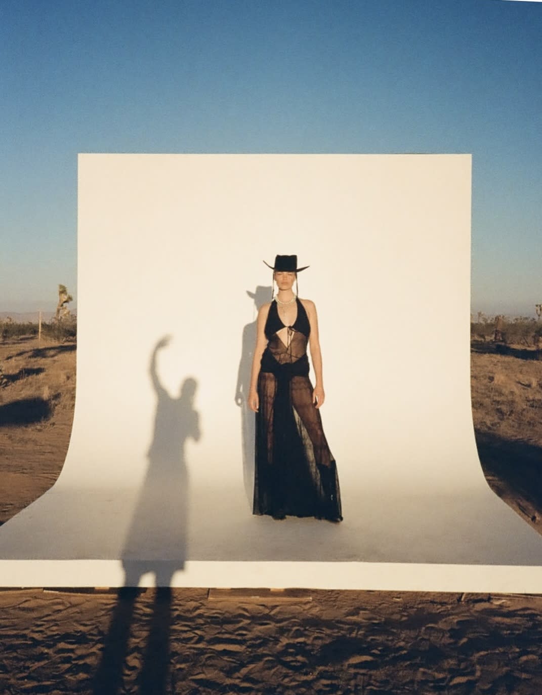 A woman poses on a white structure while holding a fan against a clear blue sky.