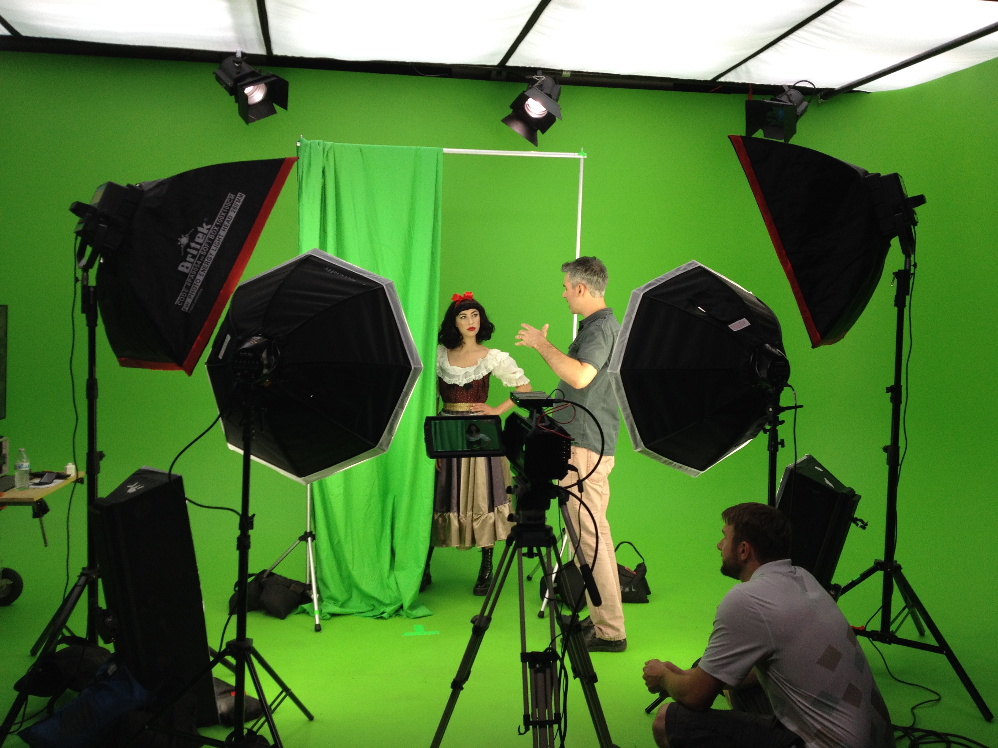 Three individuals are setting up a green screen for a video shoot in a studio.