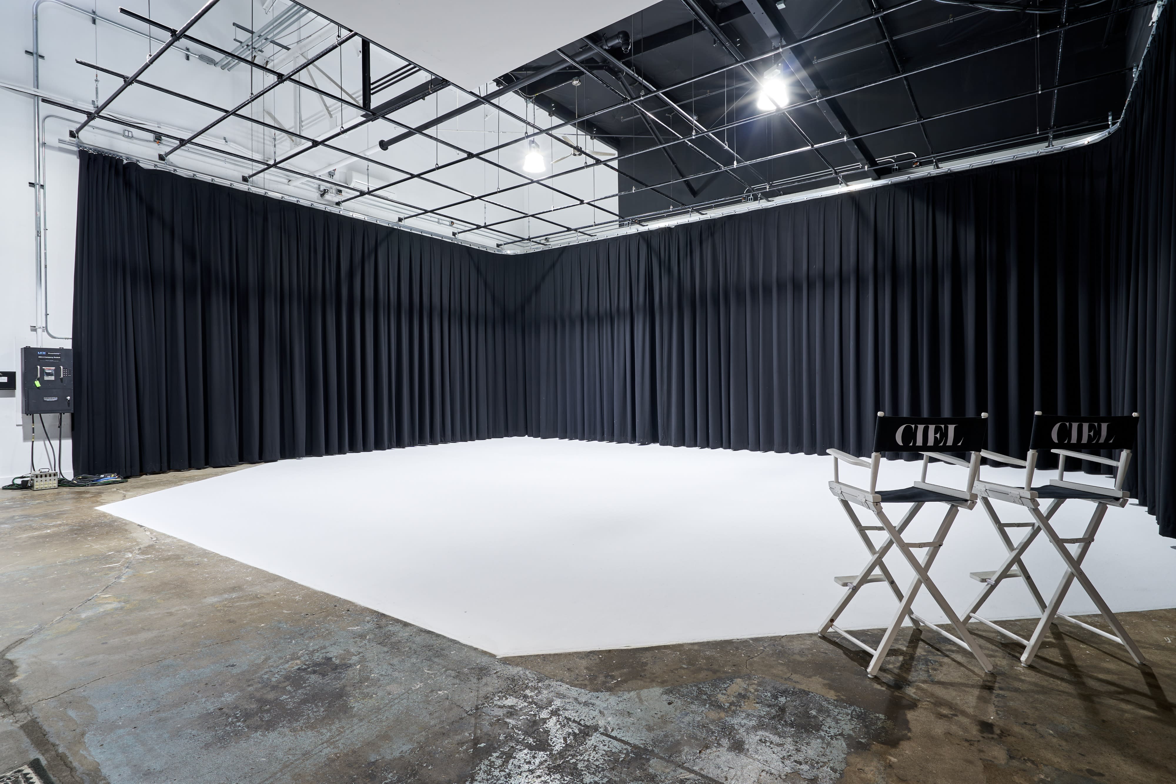 A video shoot is in progress in a spacious, well-lit studio with two crew members operating cameras while a third person performs in the center.
