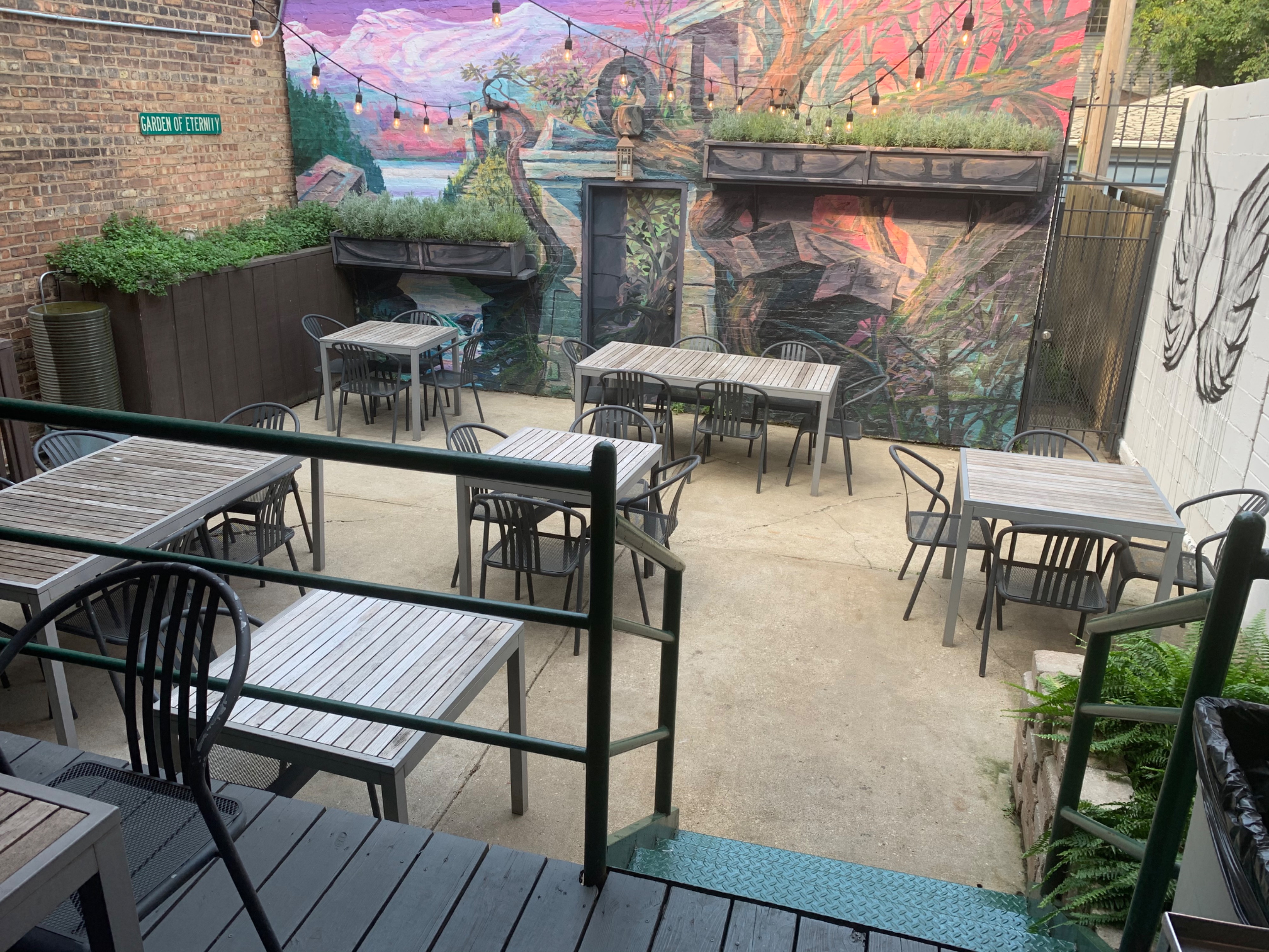 The outdoor patio features several tables and chairs arranged beneath string lights and murals, ready for a party.