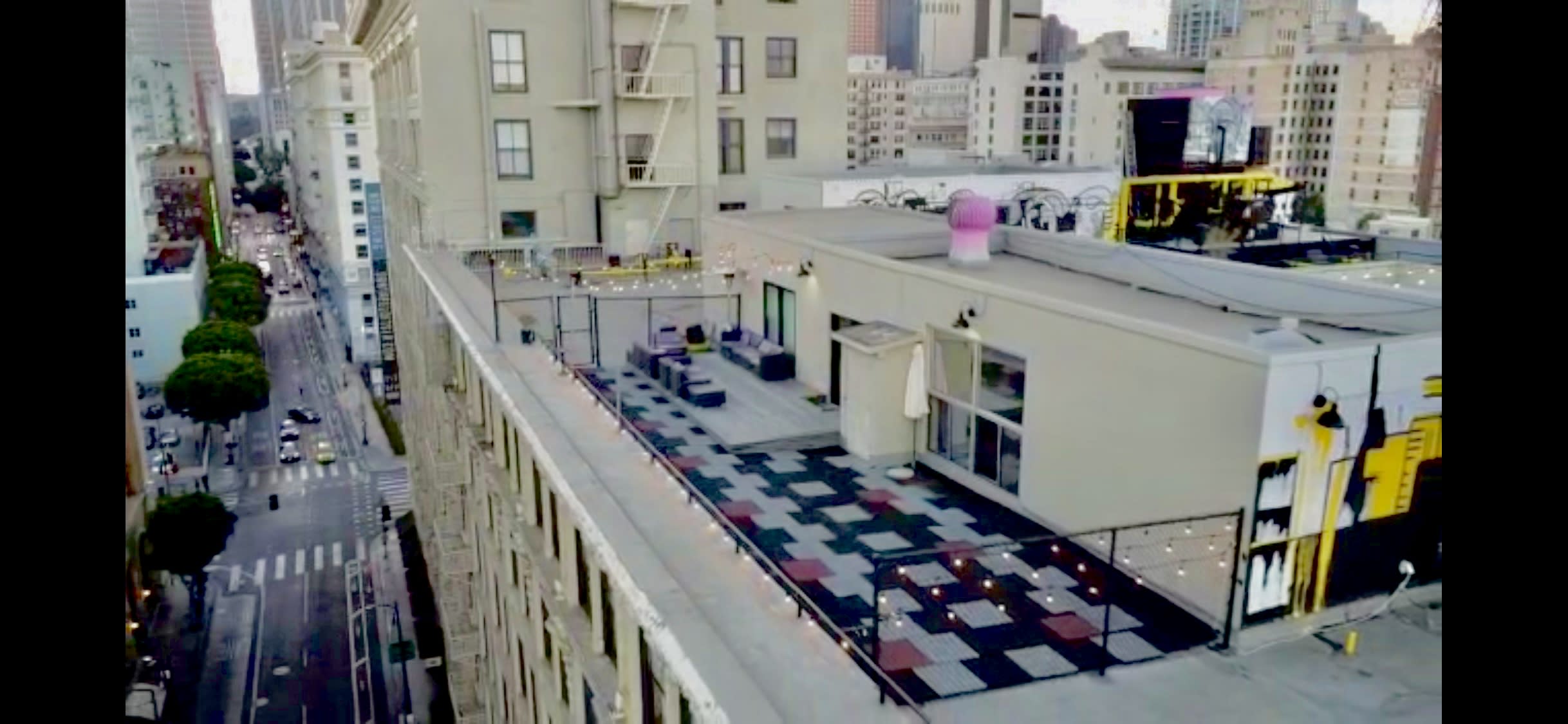 A rooftop birthday party is set up with seating and gift bags against an urban skyline at sunset.