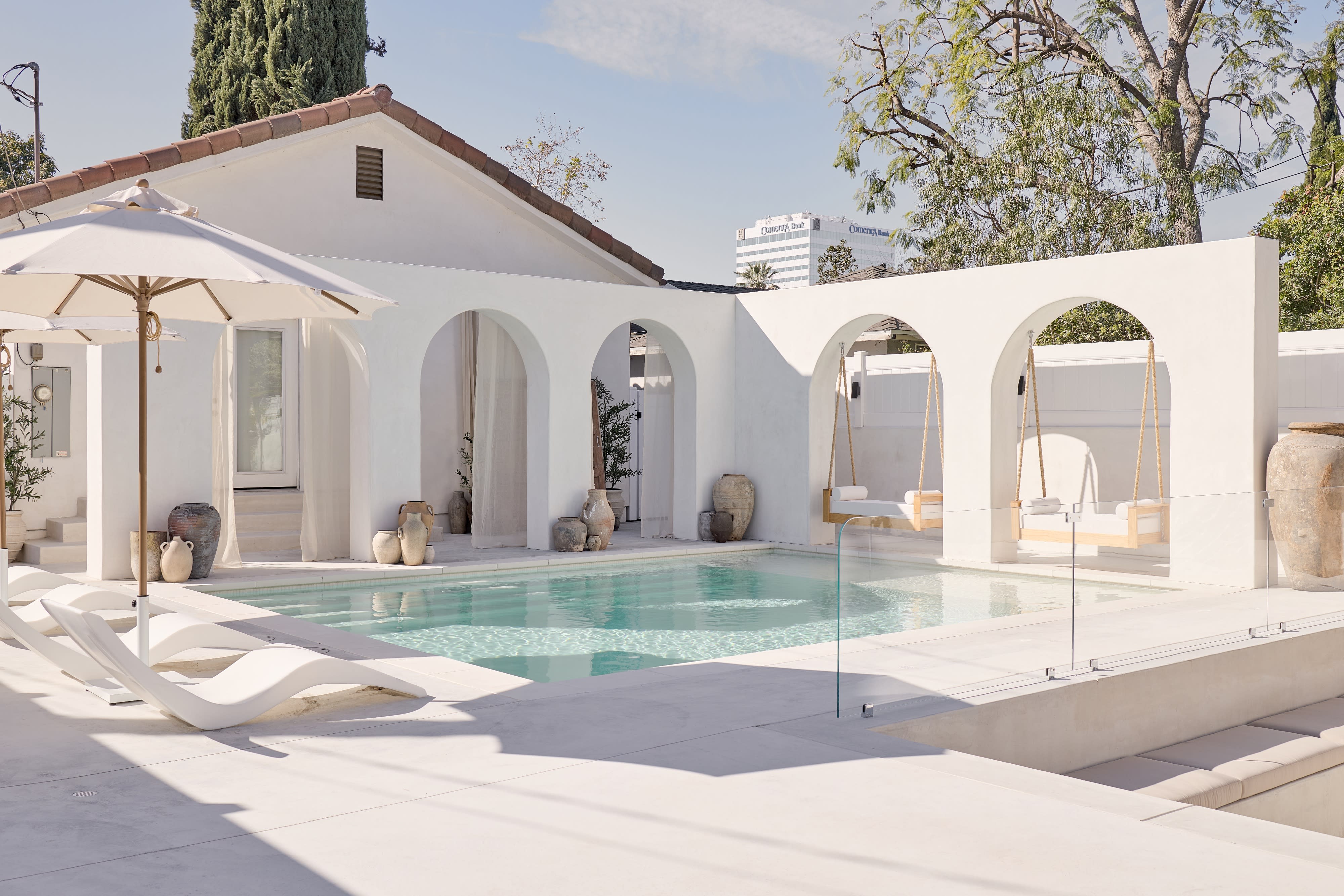 The scene features a bright outdoor pool area surrounded by white arches and decorative pottery, with an umbrella providing shade.