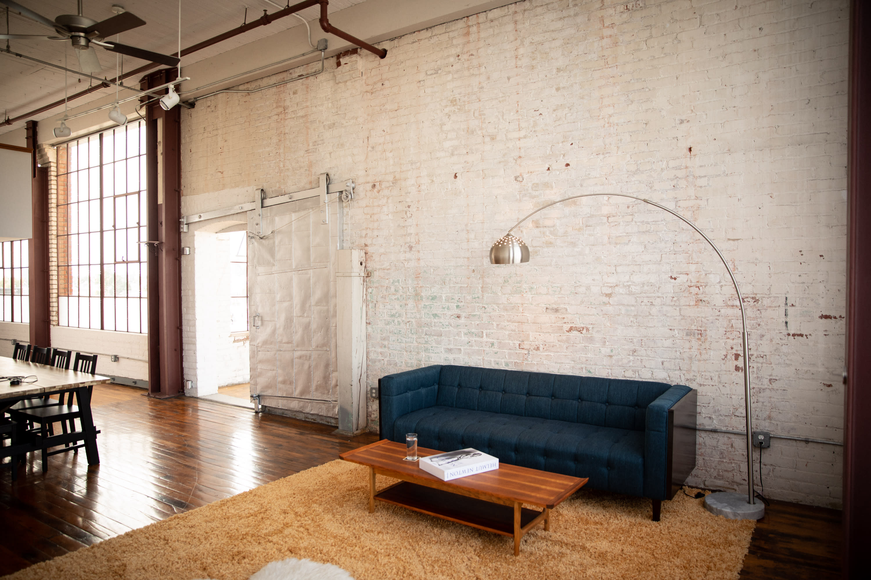 A woman prepares floral arrangements and citrus drinks in a bright workshop space filled with natural light.