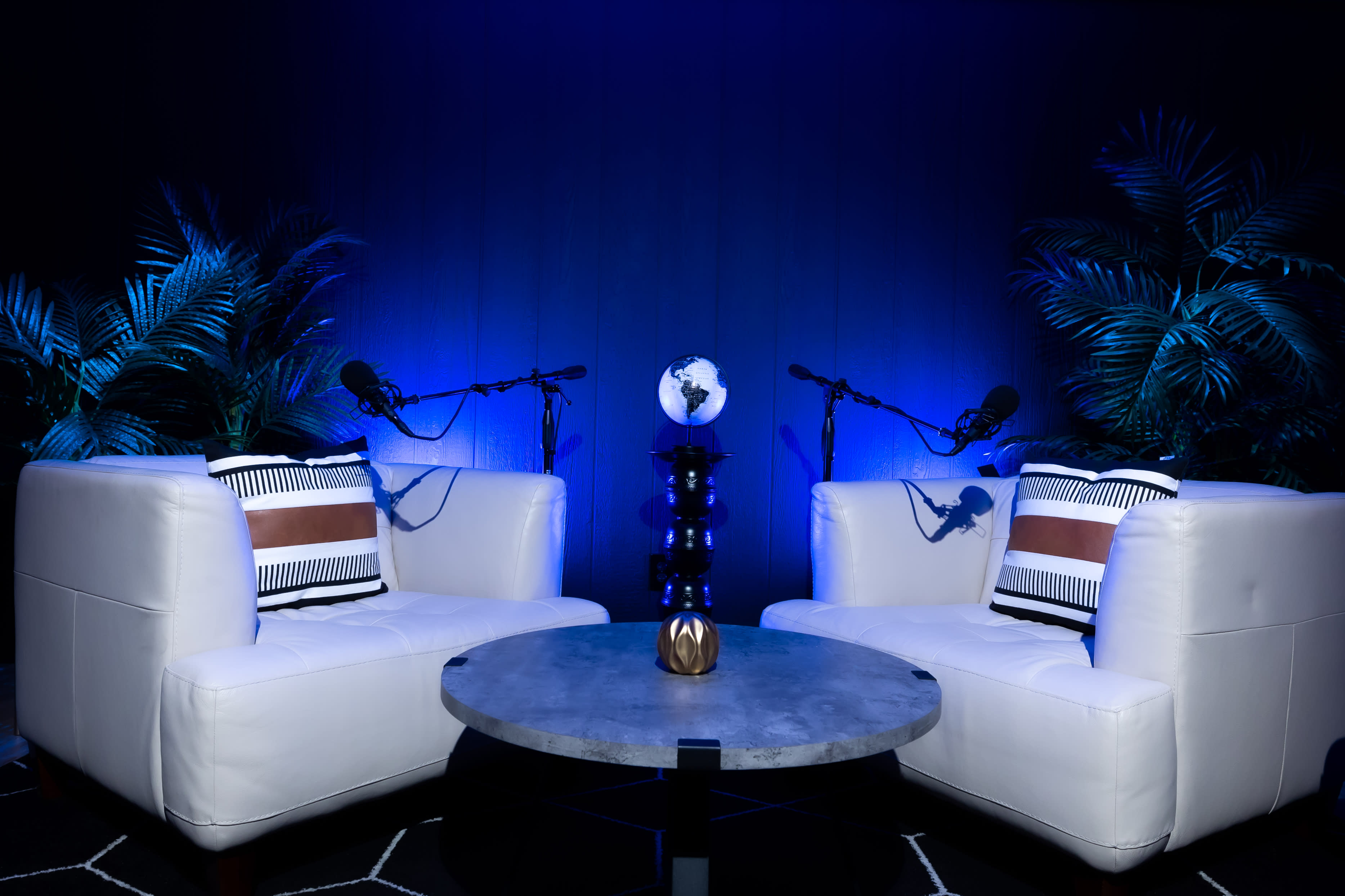 Two individuals engage in a podcast recording, discussing topics while seated in modern chairs surrounded by indoor plants and recording equipment.