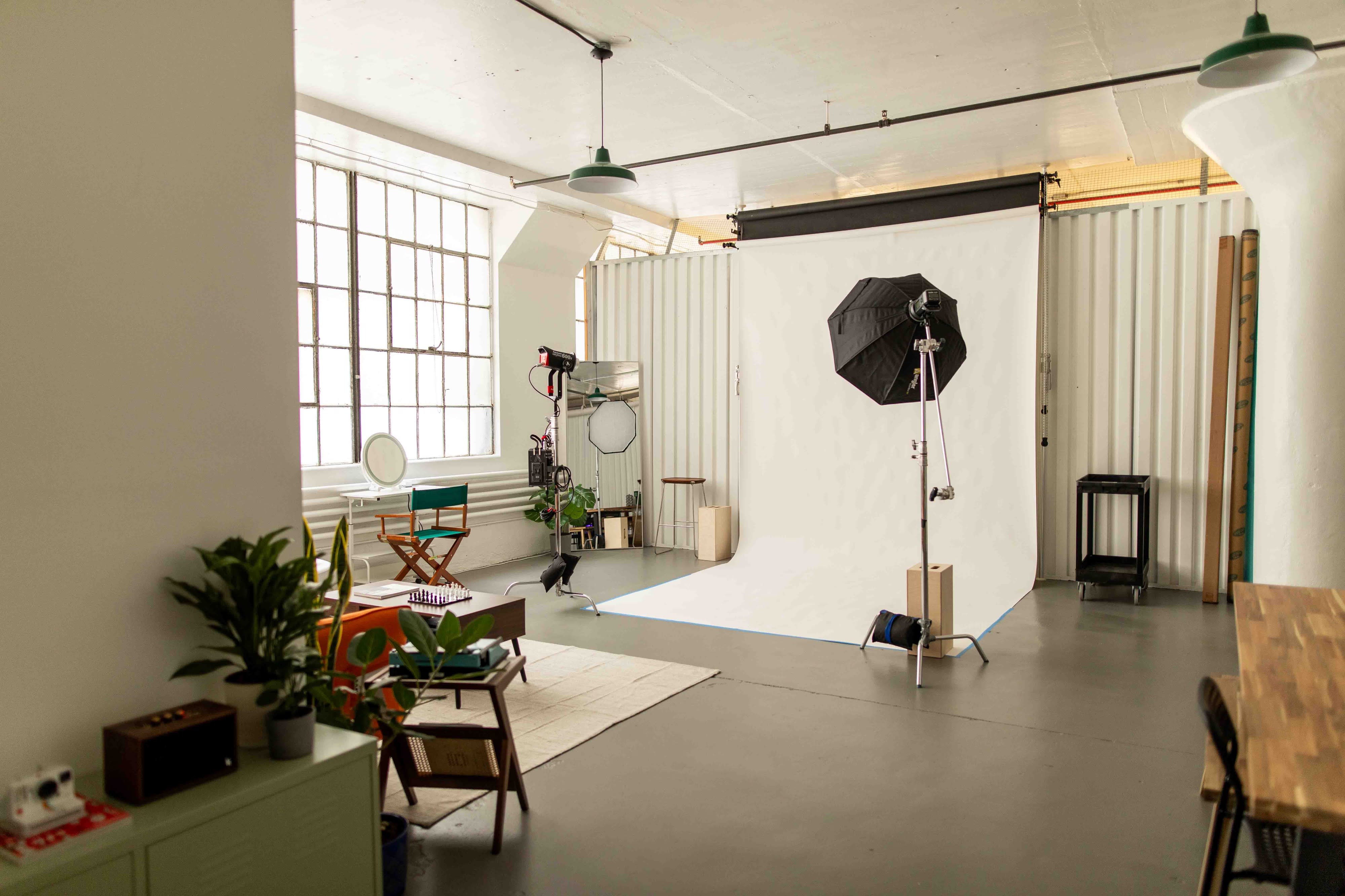A camera is set up in front of a person sitting on an orange couch in a brightly lit studio for a video interview.