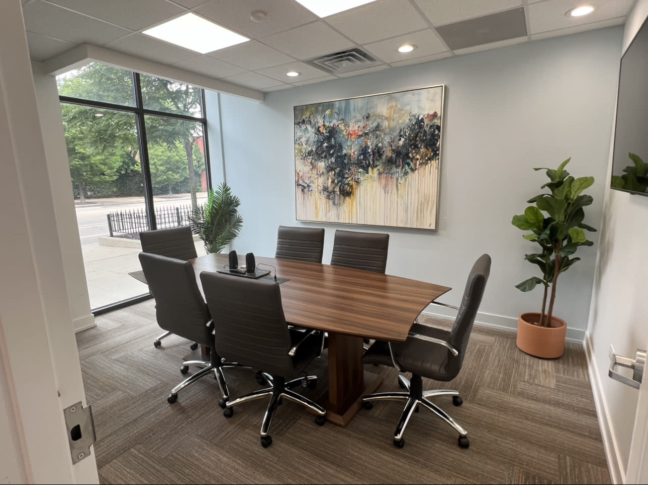 A film crew records a meeting where four people discuss a project around a conference table, with a camera and lighting setup in the background.