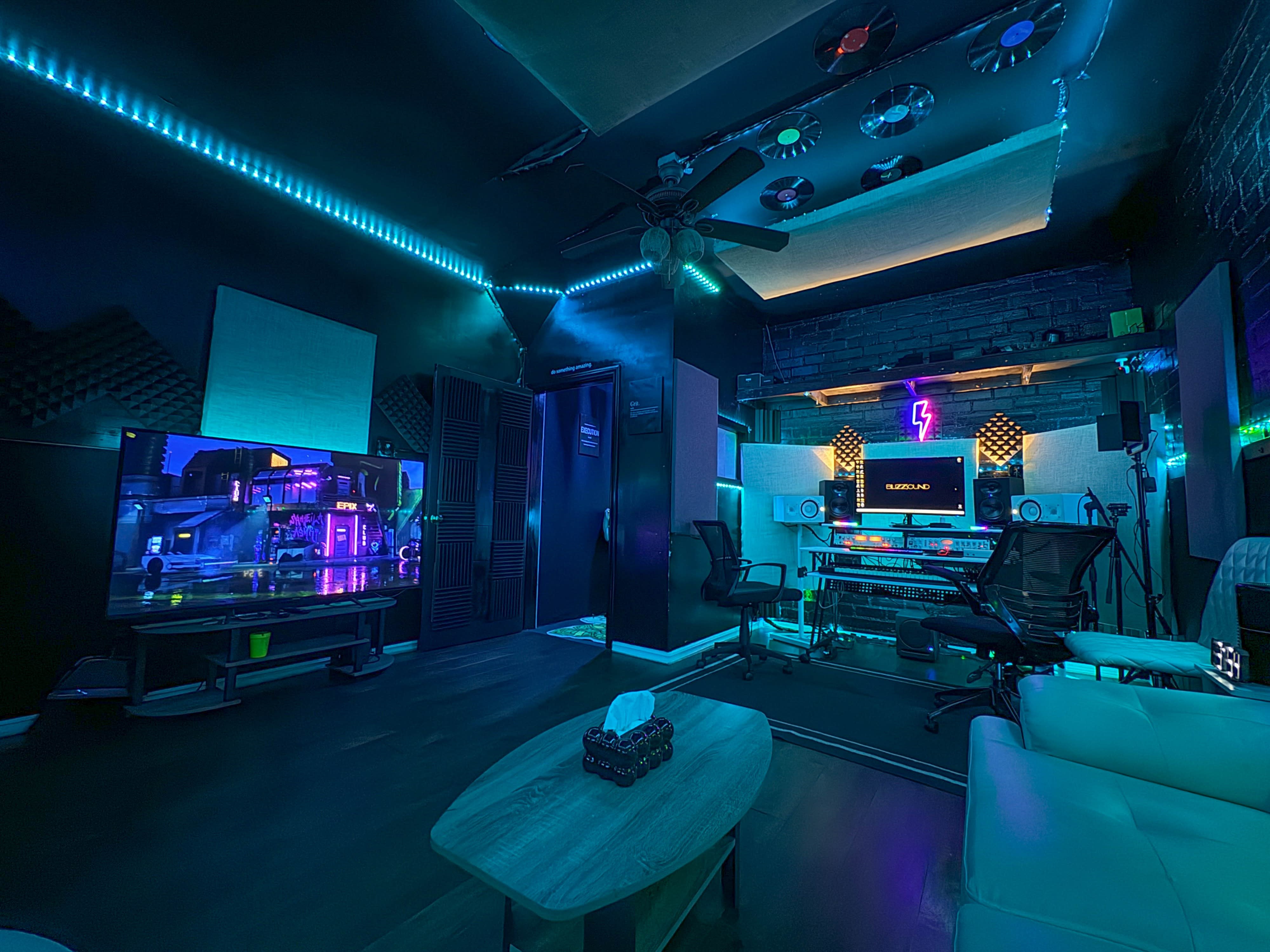 Two individuals are working in a music recording studio, with one sitting at a computer and the other playing a musical instrument.
