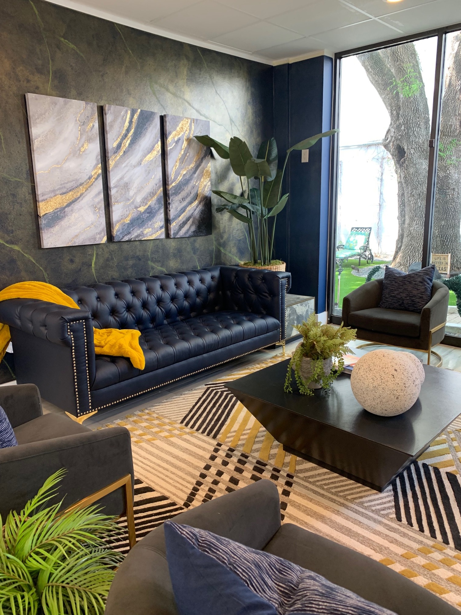 A woman in a green blouse poses thoughtfully on a blue couch in front of abstract wall art.