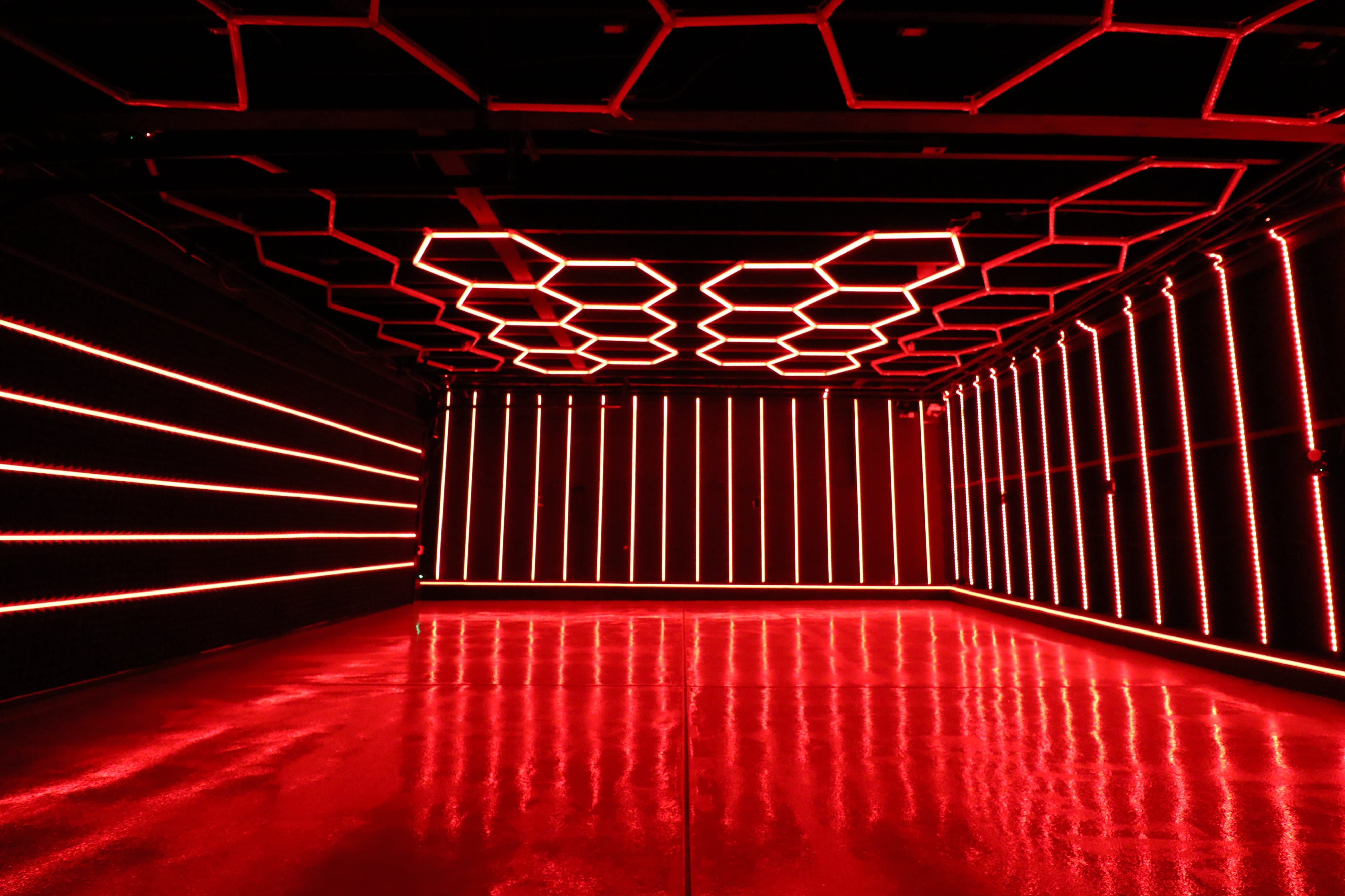 A performer skillfully manipulates flaming poi in a dark room illuminated by neon lights.