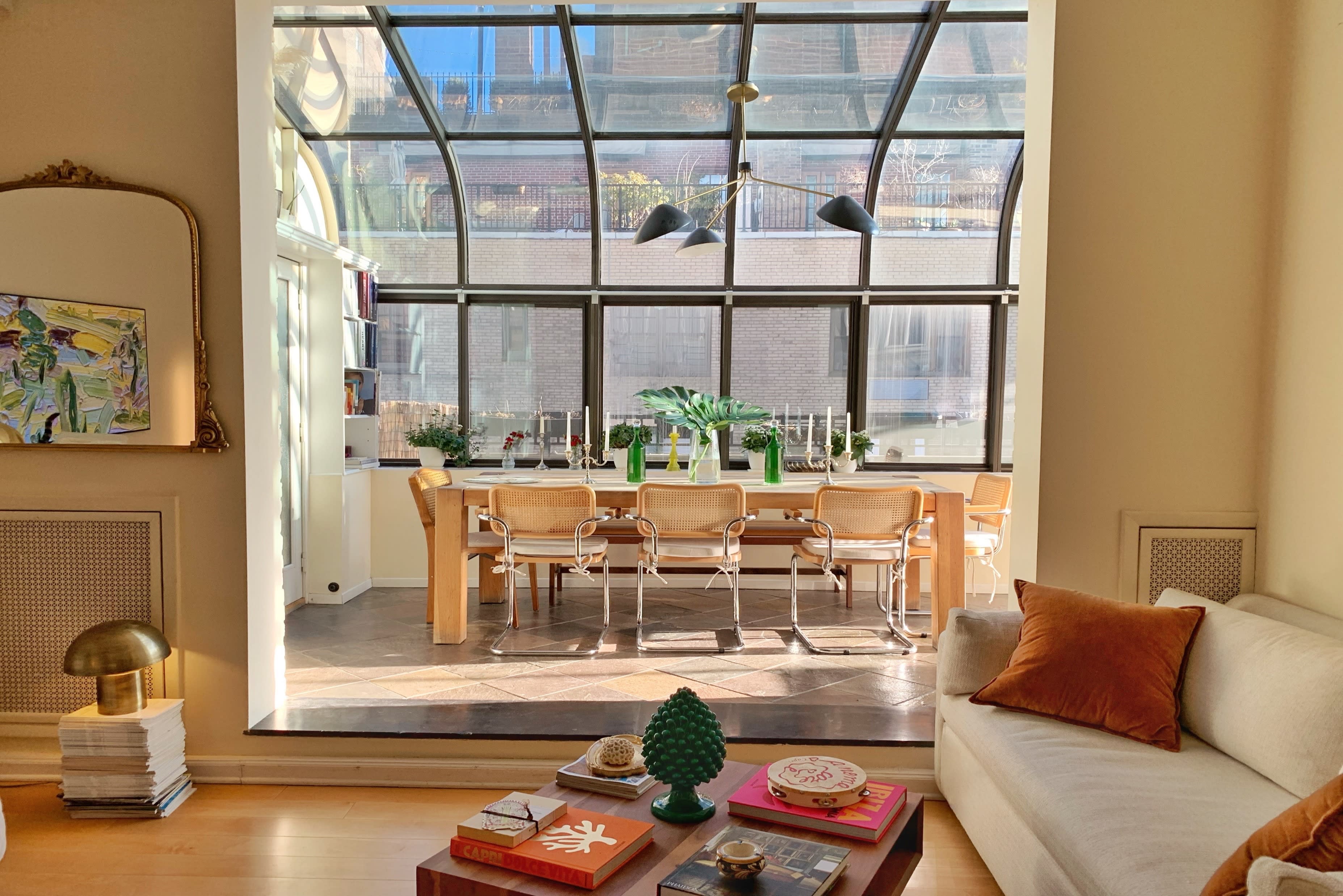 A bright sunroom features a wooden dining table, indoor plants, and comfortable seating, creating an inviting space for a photo shoot.