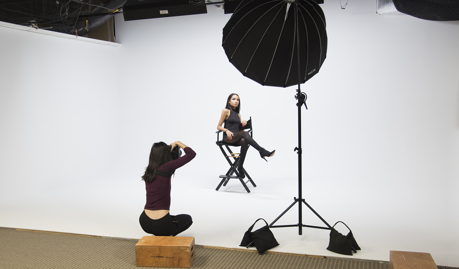 A person exhales smoke while posing for a video shoot against a plain background.