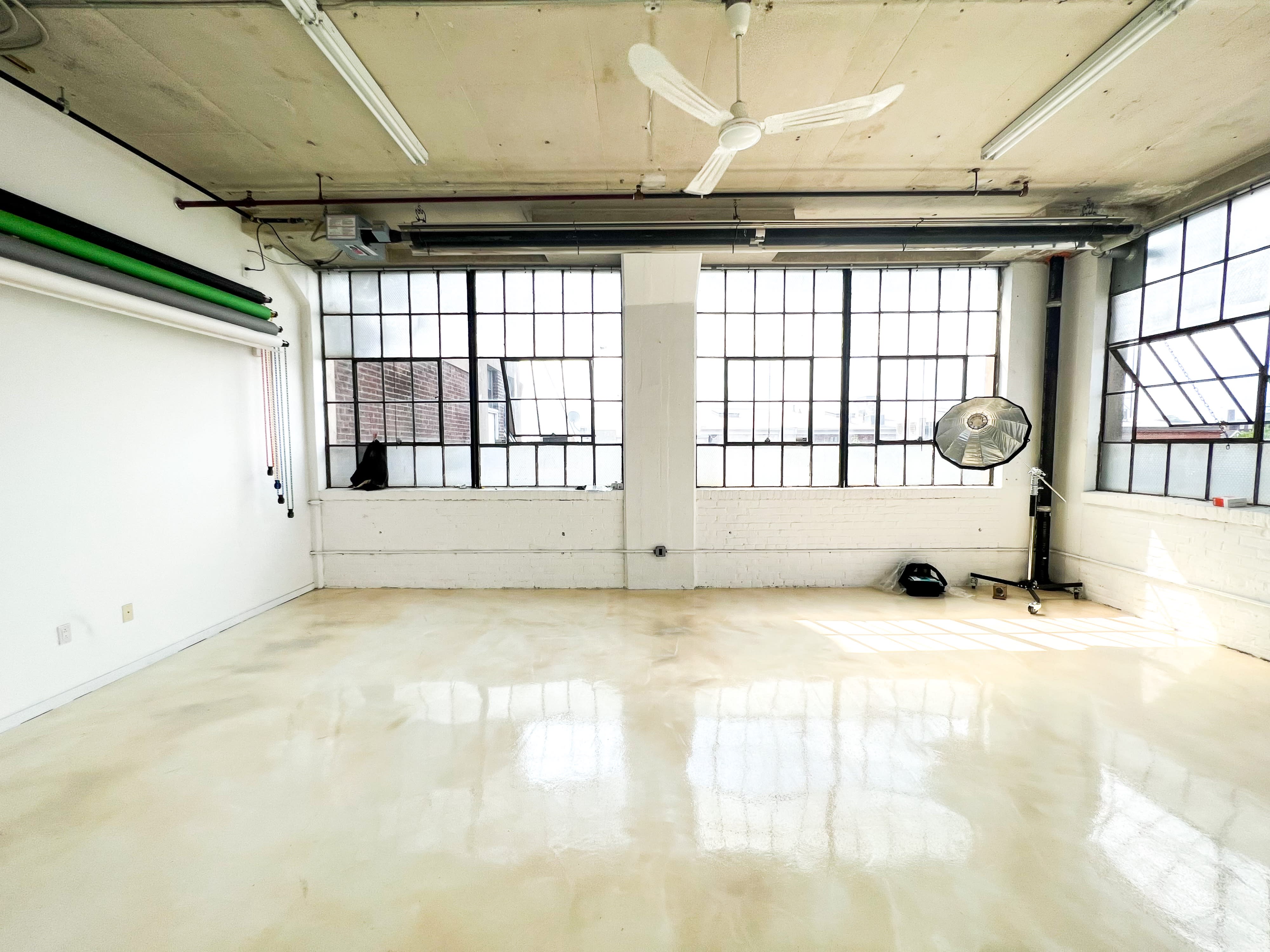 The image showcases a spacious photography studio with large windows, polished floors, and a backdrop stand set up for a photoshoot.