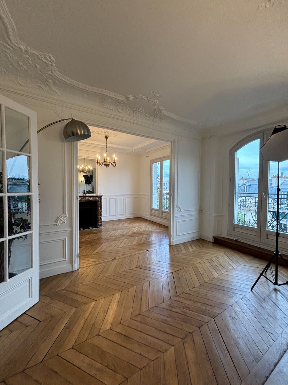 A photoshoot takes place in a room featuring a mirror, a decorative fireplace, and various equipment set up in the background.