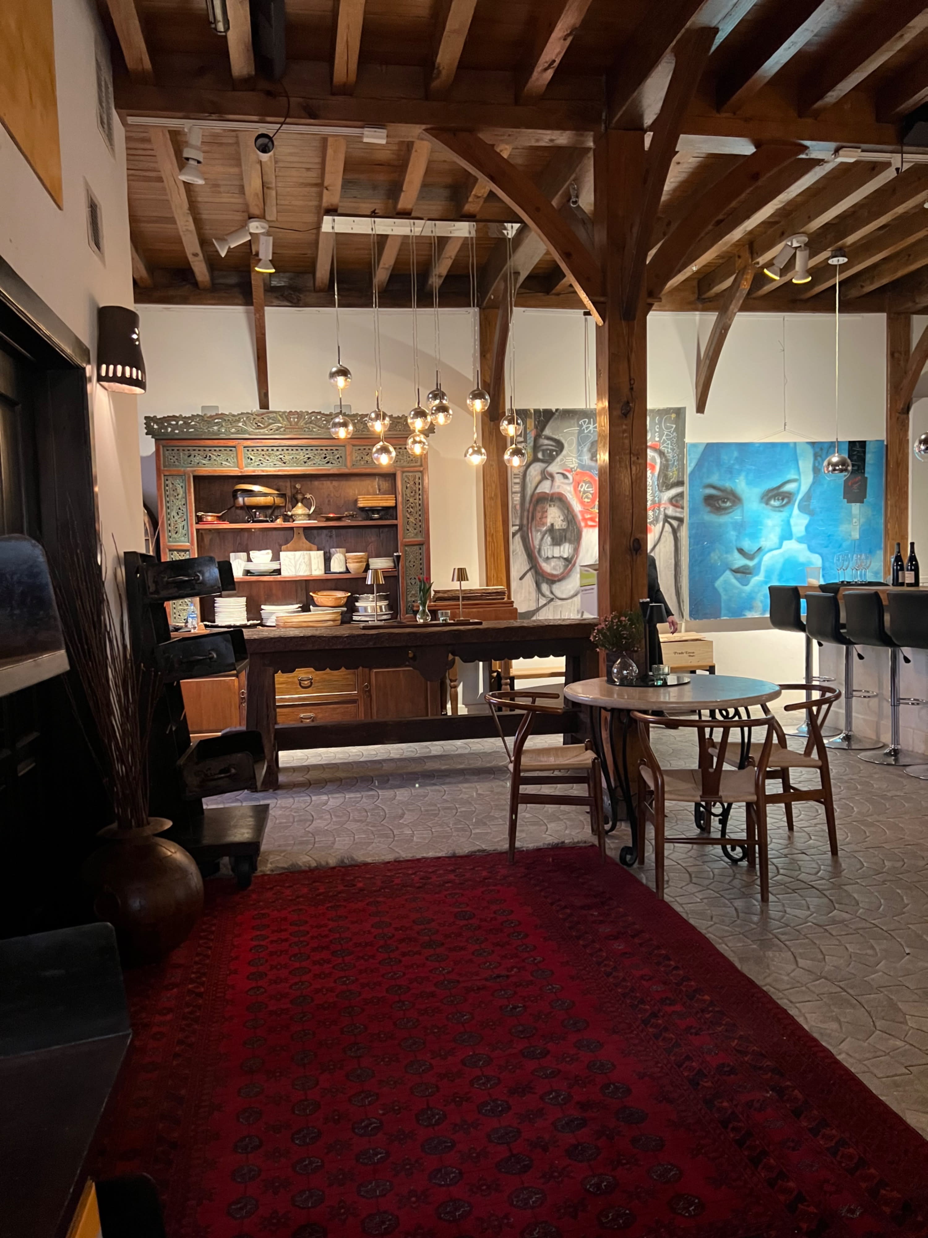 A group of people gathers around a buffet table, enjoying food and drinks in a cozy setting with wooden beams and warm lighting.