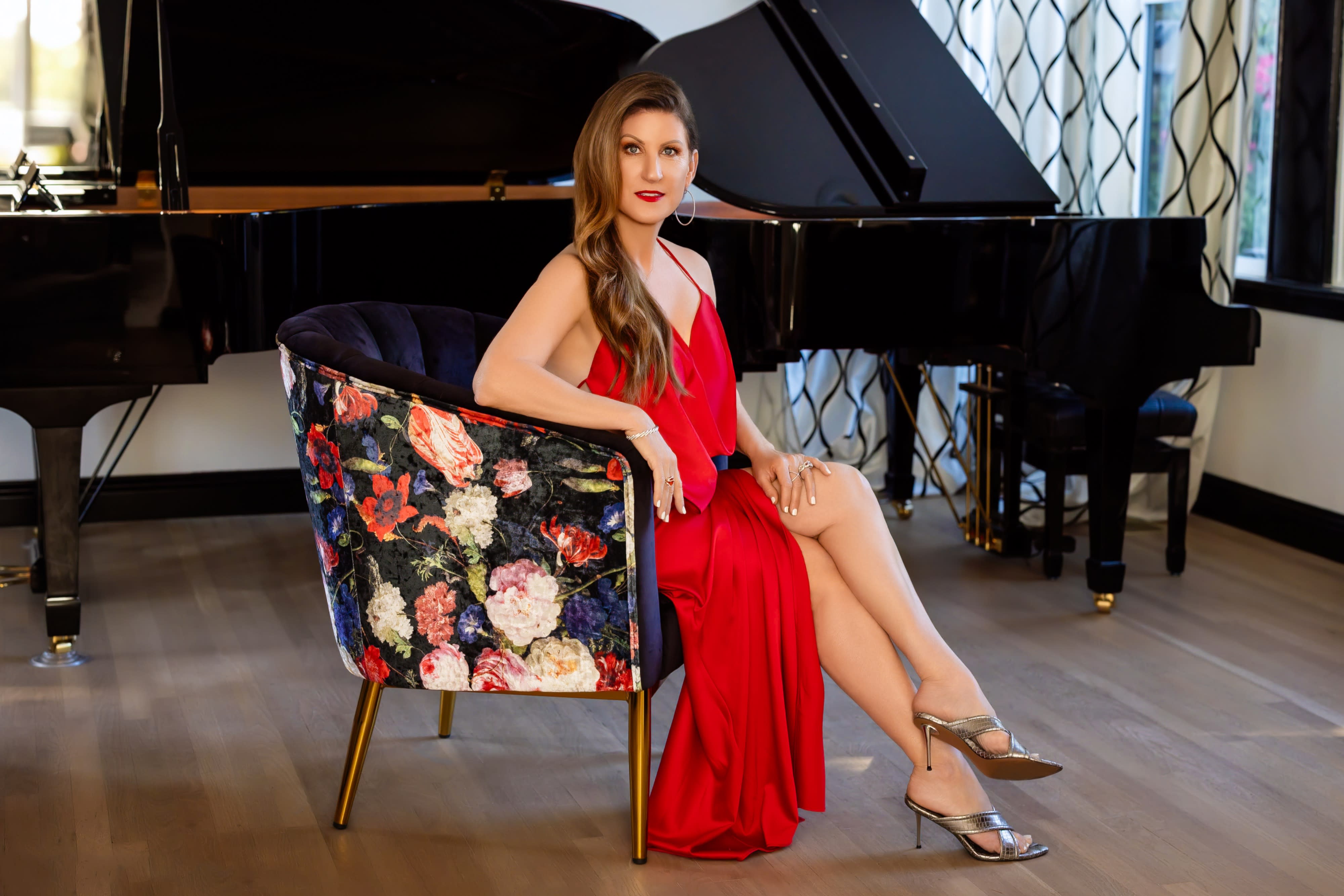 The woman poses elegantly with a bottle of perfume, showcasing her makeup and hairstyle against a backdrop of decorative lighting.