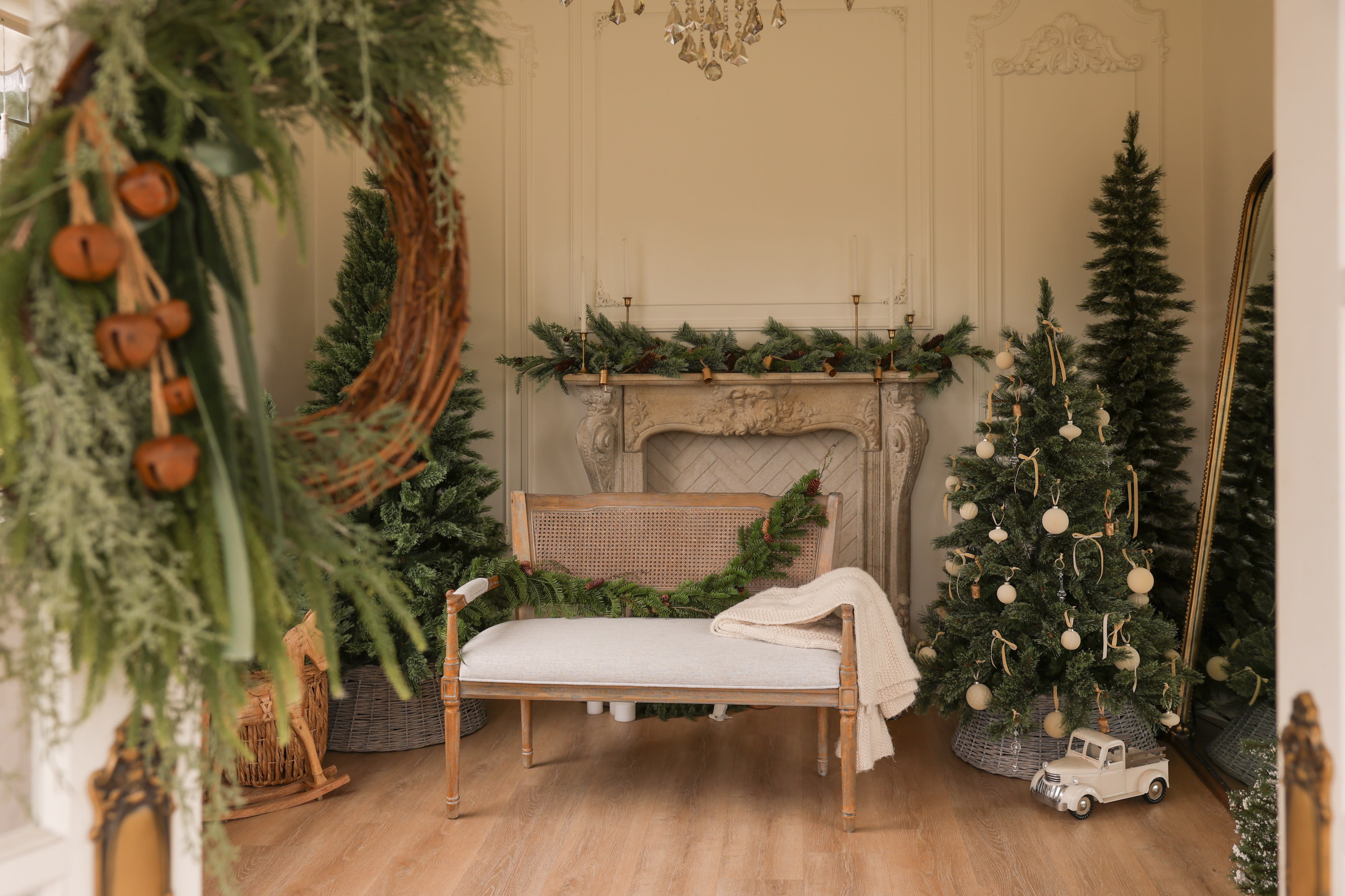 A cat sits on a bench in front of a decorative fireplace adorned with greenery and candles, while a frosted Christmas tree stands nearby.