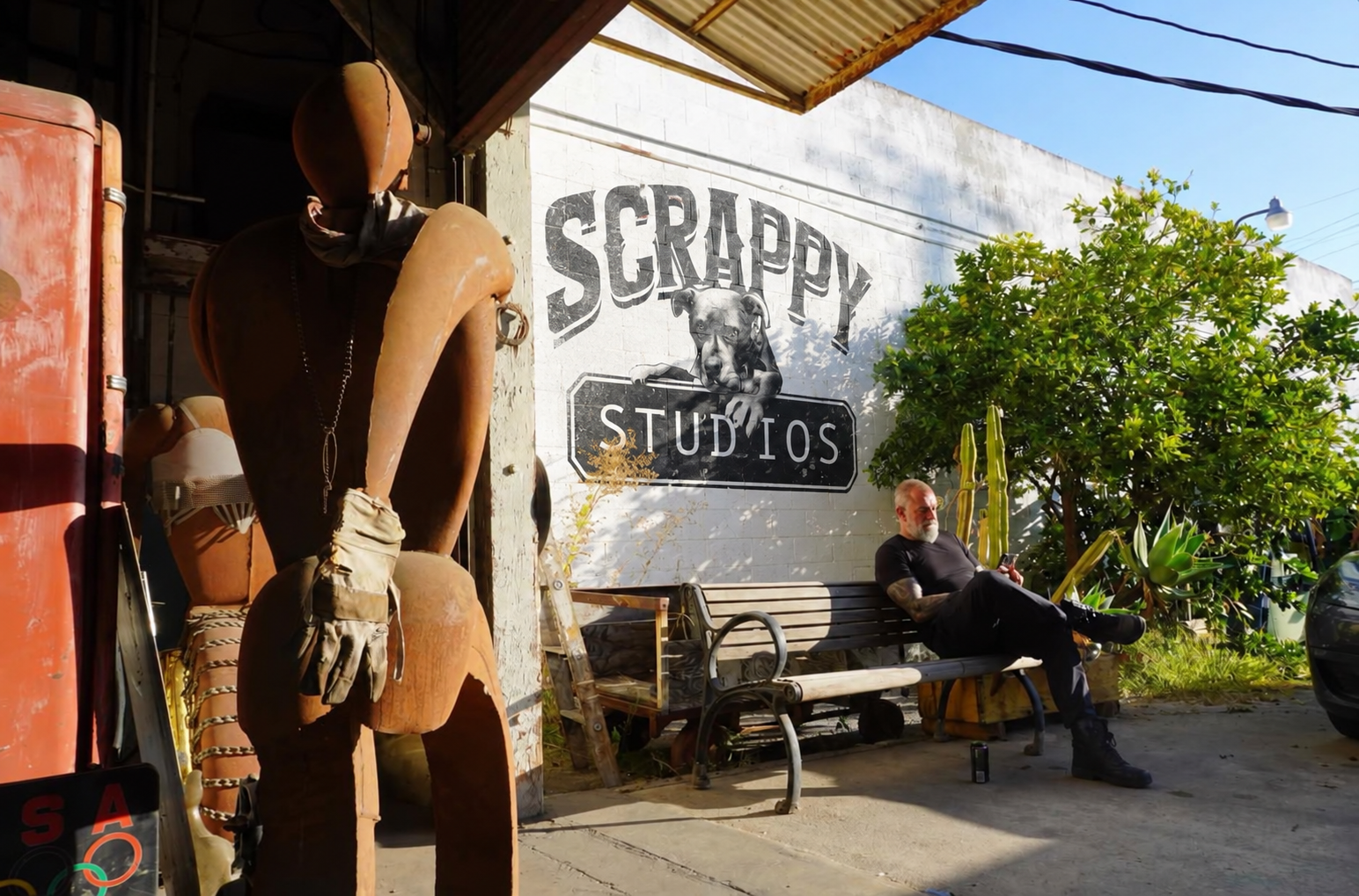 A person wearing sunglasses relaxes on a chair during a photoshoot in a vintage-themed setting.