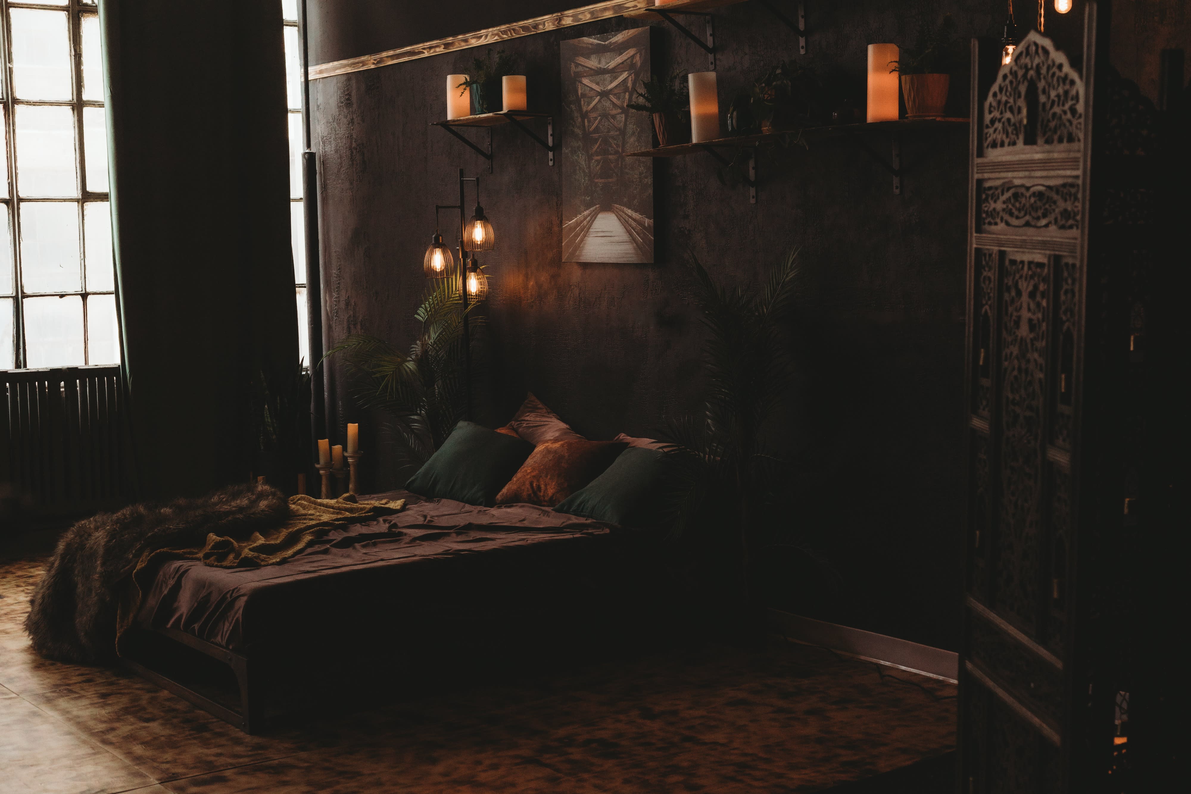 A woman dressed in lingerie sits on a bed, holding a candle while surrounded by dim lighting and dark decor.